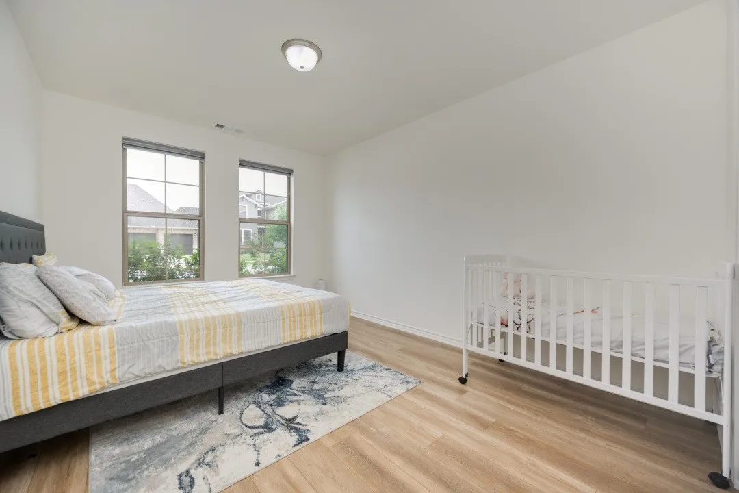 Bright room featuring wood-finish flooring, two large windows, neutral wall tones, and a flush-mount ceiling light