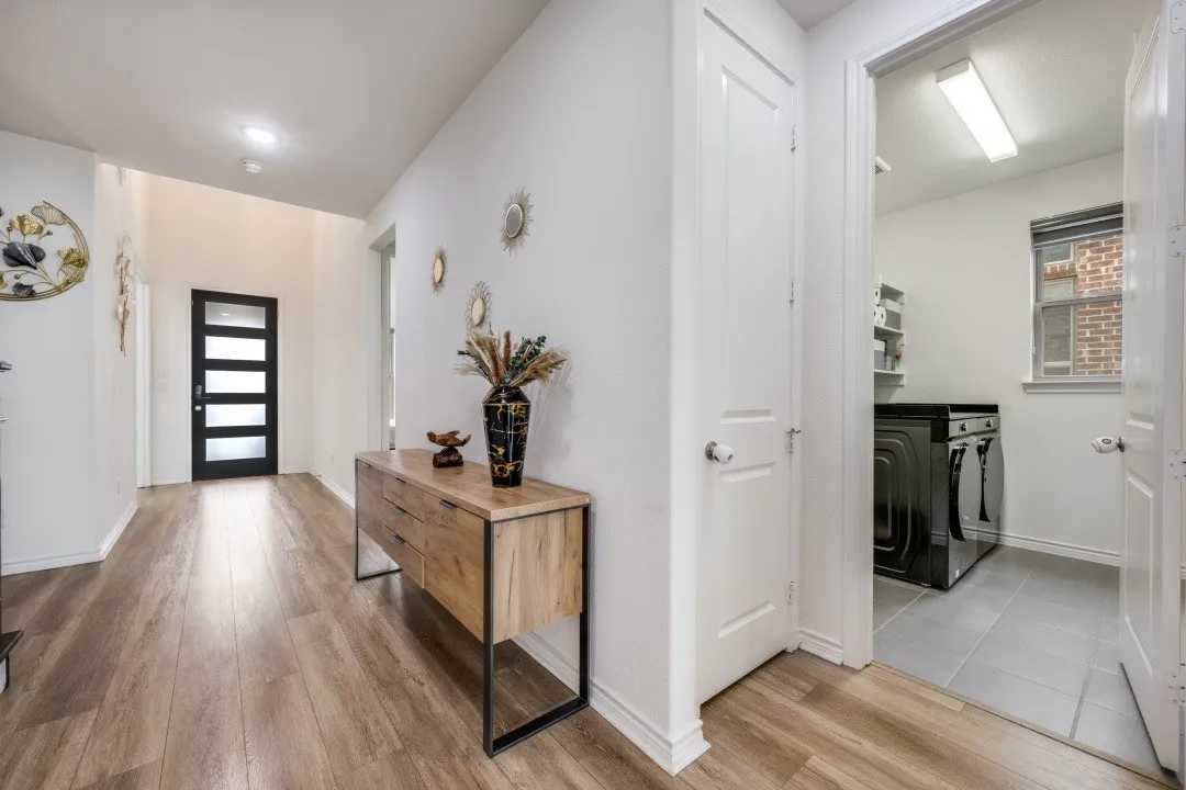 Entryway with wood-finish flooring extending into a bright utility room featuring tile flooring, a window, and built-in shelving