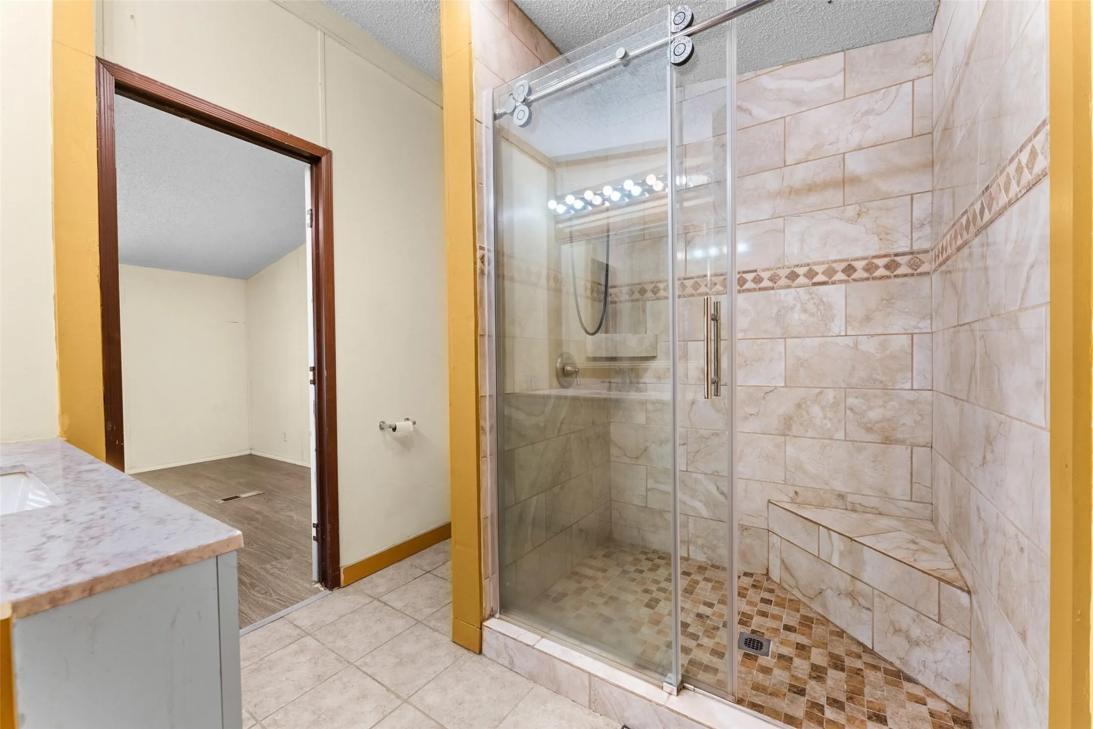 Glass-enclosed shower with a sliding barn door style entry, built-in bench, and tiled walls with decorative accent banding