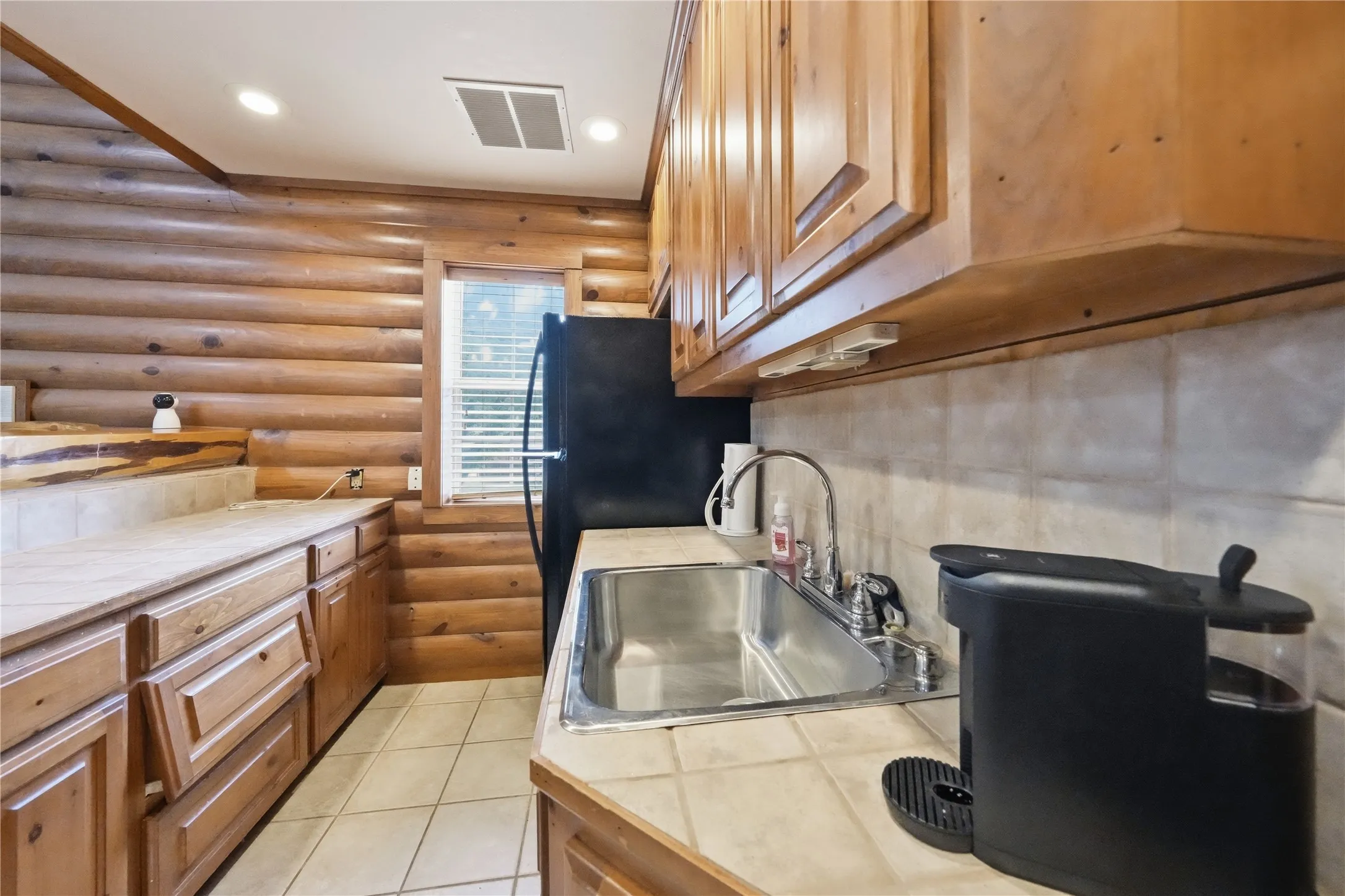 Kitchen featuring natural wood log walls, light wood cabinetry, and a tile backsplash