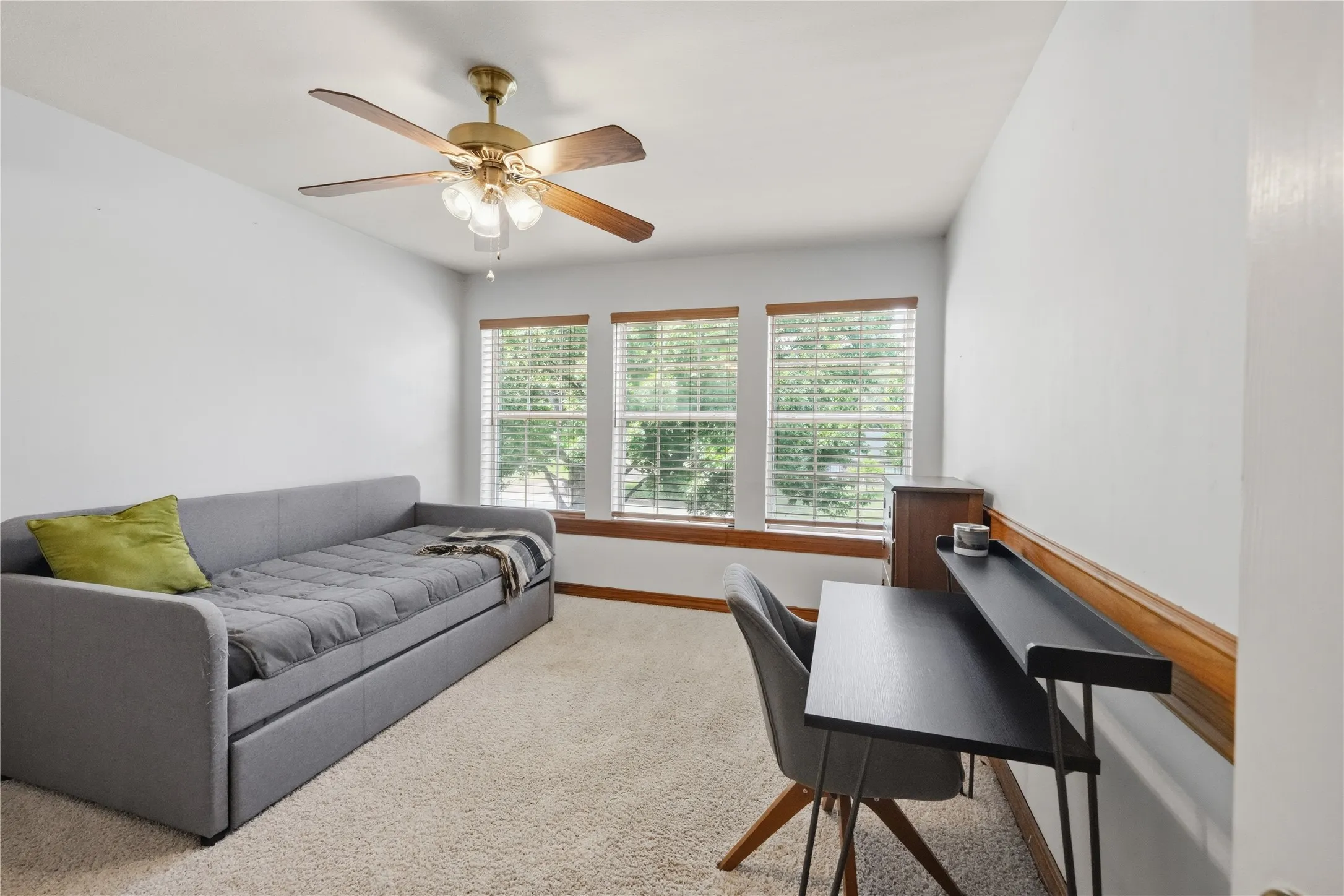 Bright room featuring three windows with blinds, wood-finish window trim, a ceiling fan with integrated lighting, and neutral carpet flooring