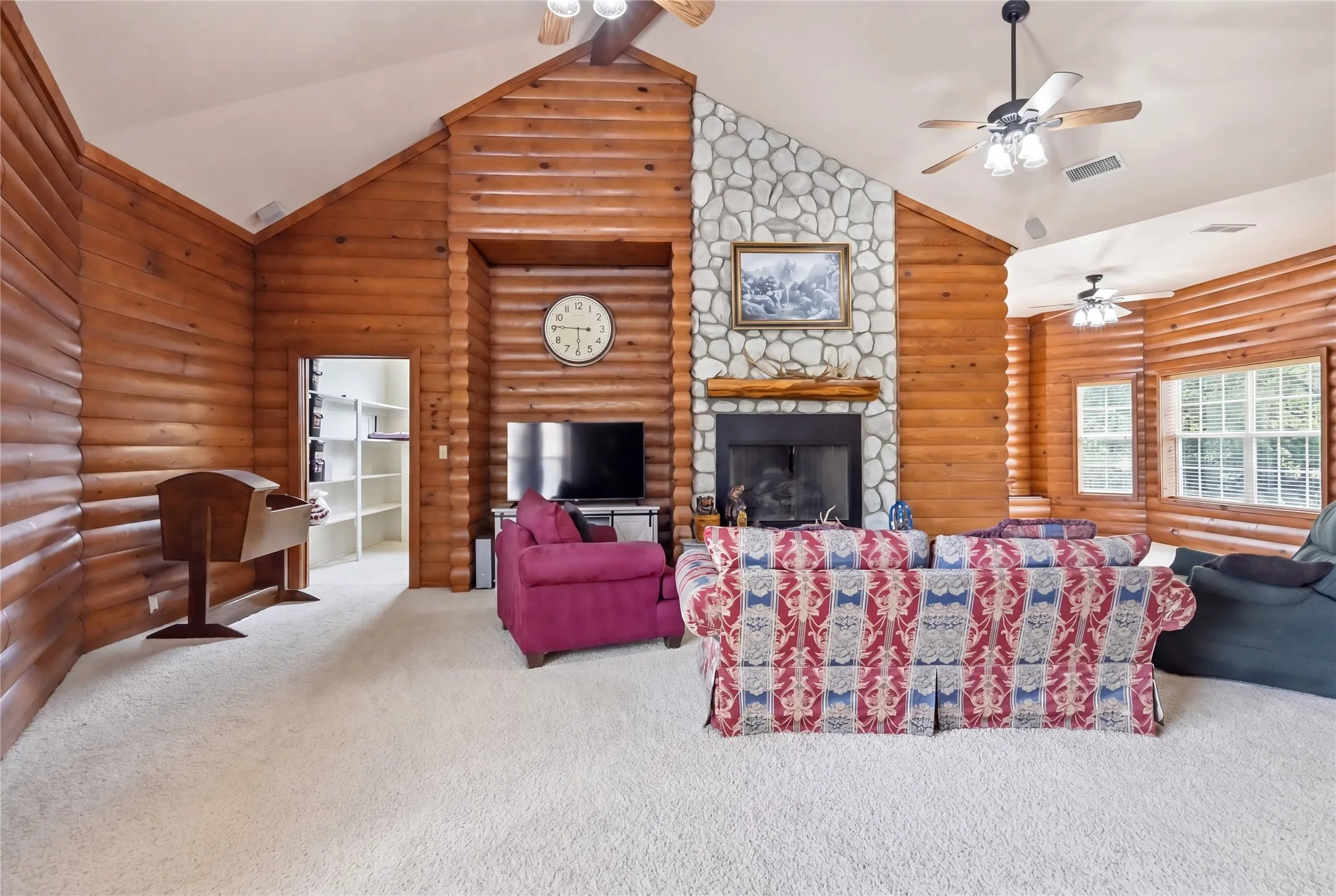 Living space featuring natural log walls, a vaulted ceiling, and light-colored carpeting