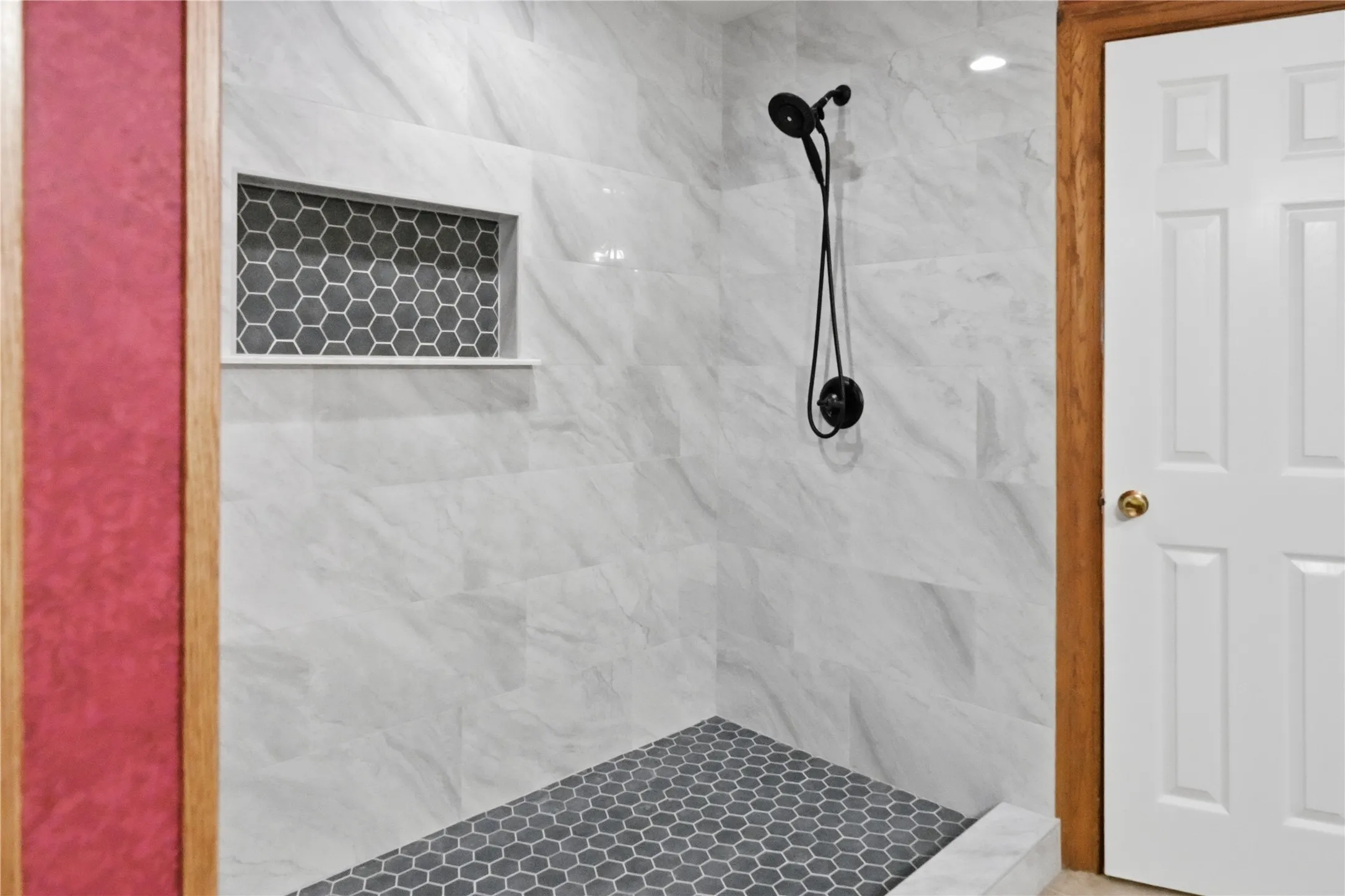 Walk-in shower featuring large format white marble-look wall tiles, dark grey hexagonal floor tiles, a recessed niche with matching hexagonal tiling, and matte black shower fixtures