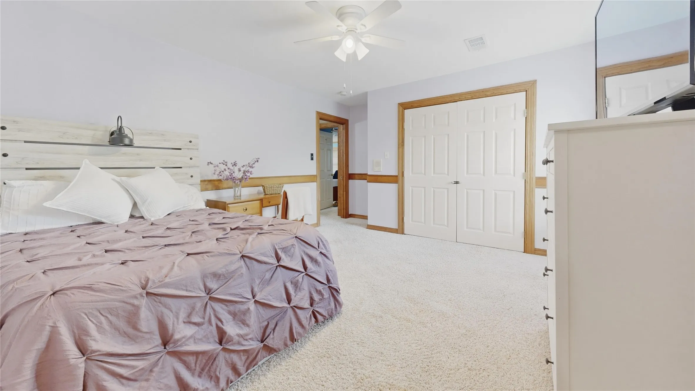 Spacious room featuring light-toned carpeting, a ceiling fan, white bi-fold closet doors with wood trim, and a doorway with wood trim