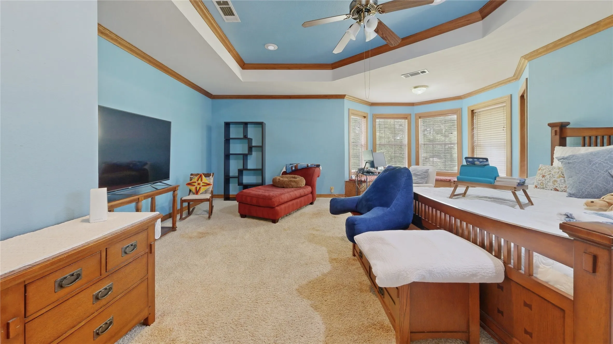 Spacious room featuring a tray ceiling with a ceiling fan, bay windows, wood-finish trim, and carpet flooring