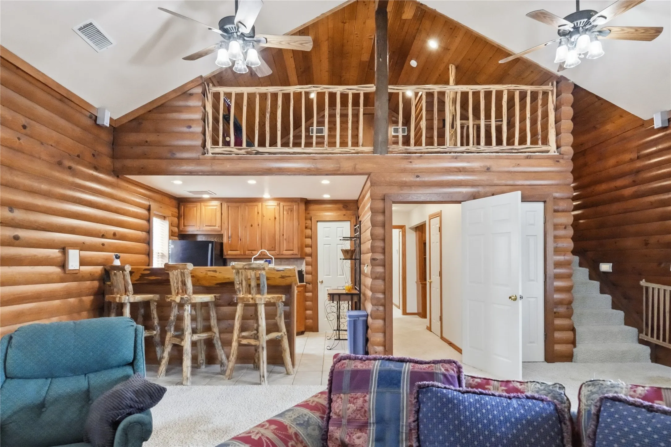 Great room featuring natural wood log walls, a vaulted ceiling, and an open loft