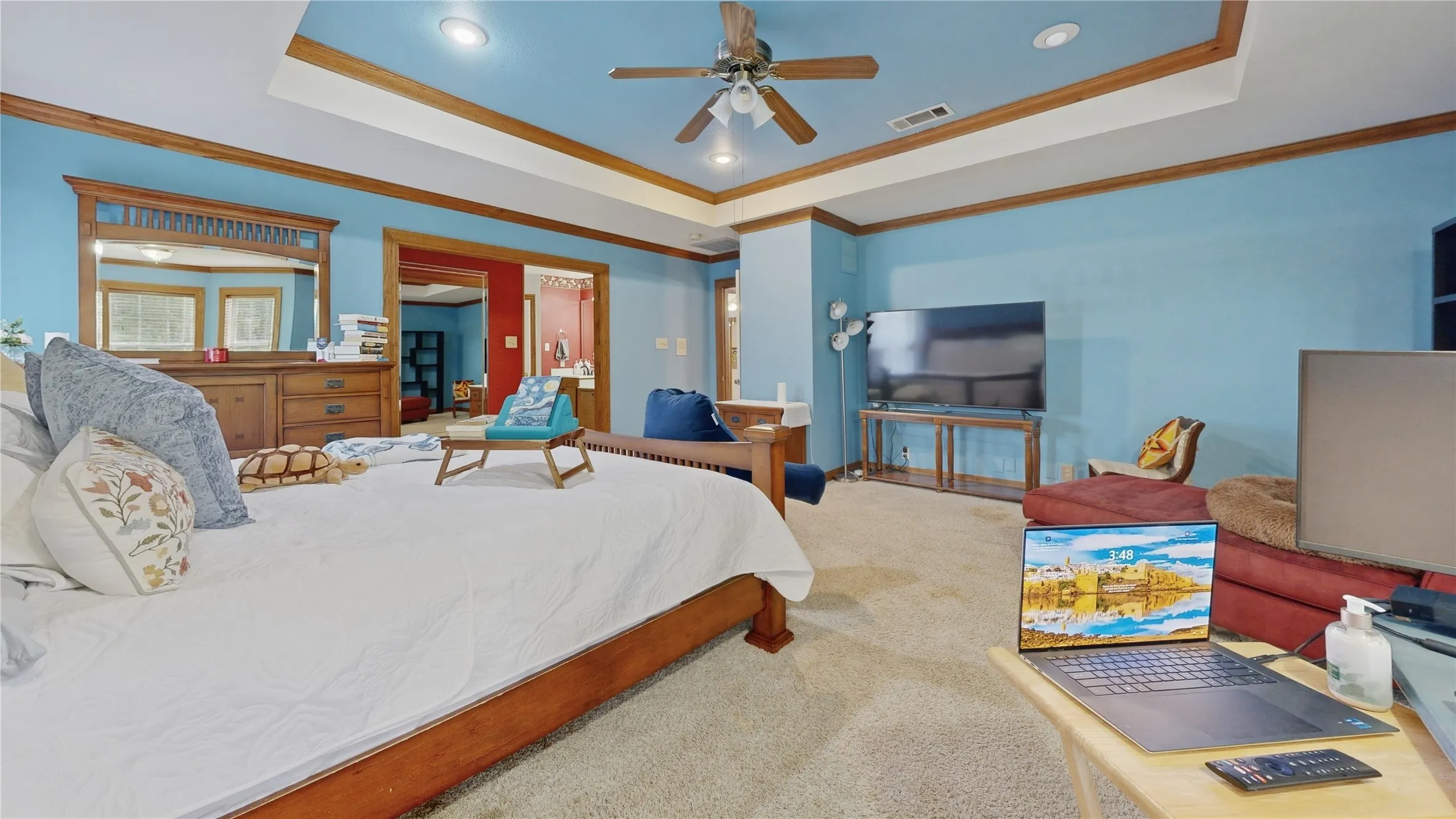 Spacious carpeted room featuring a ceiling fan, recessed lighting, and a tray ceiling with wood-finish trim