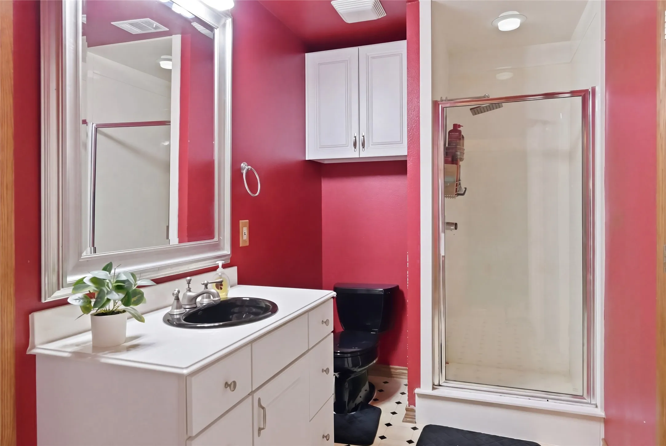Bathroom featuring a white vanity with a black oval sink, framed mirror, and a glass-enclosed shower