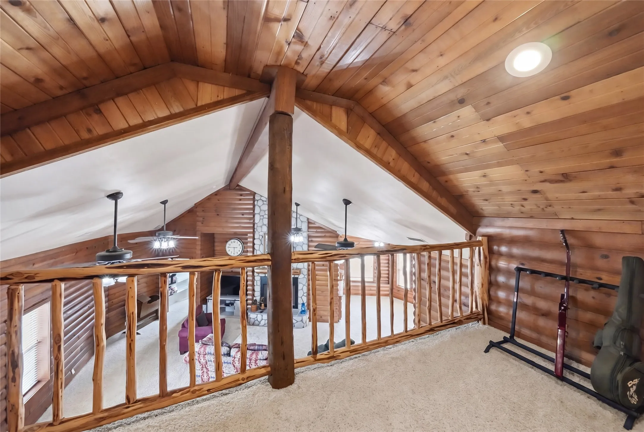 Loft area featuring natural wood plank ceiling, exposed log beams, and a wood railing overlooking the living space below