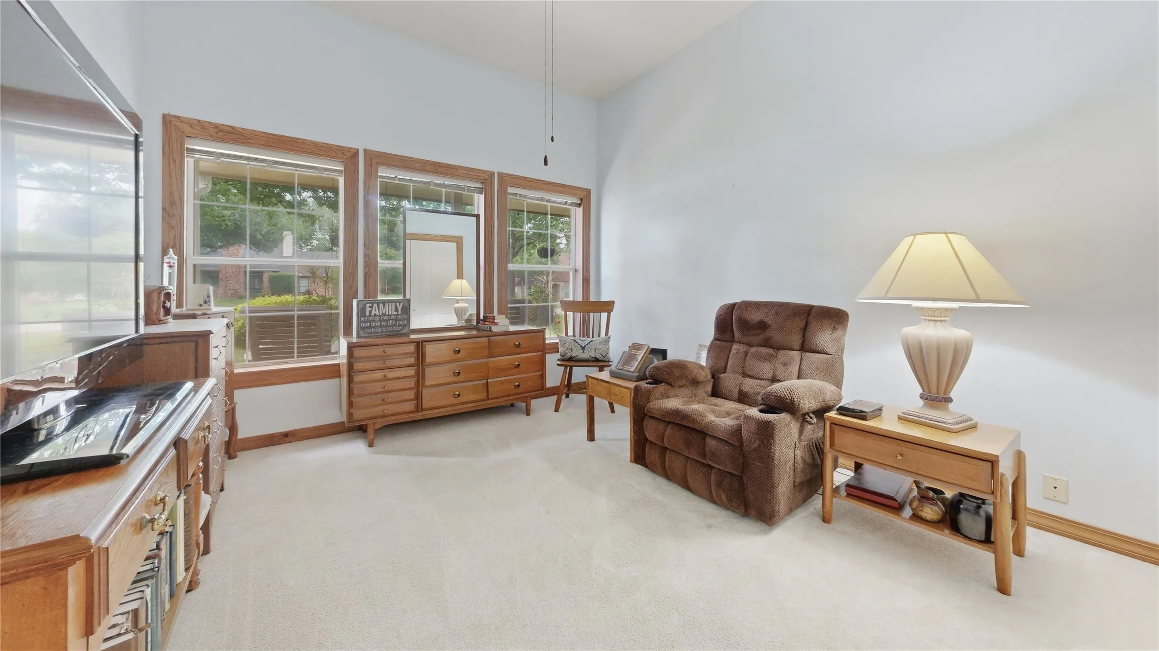 Spacious room featuring vaulted ceilings, light-colored carpeting, and multiple windows with wood-finish trim