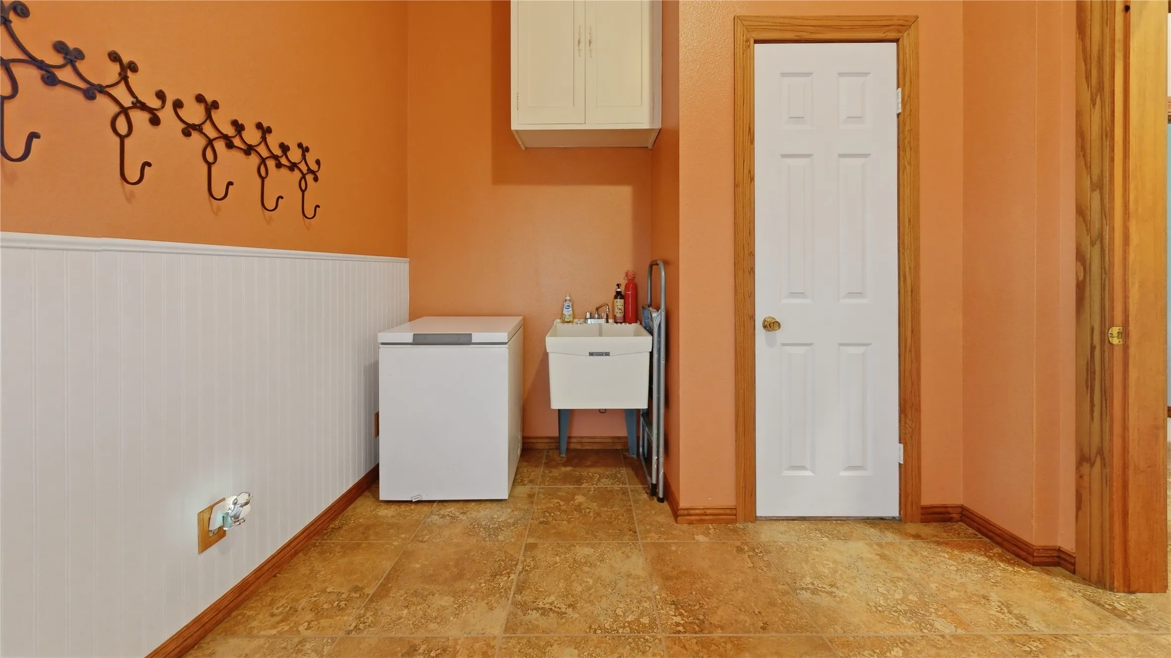 Mud room off the garage entrance featuring a utility sink, wall-mounted cabinetry, durable tile flooring, and wainscoting