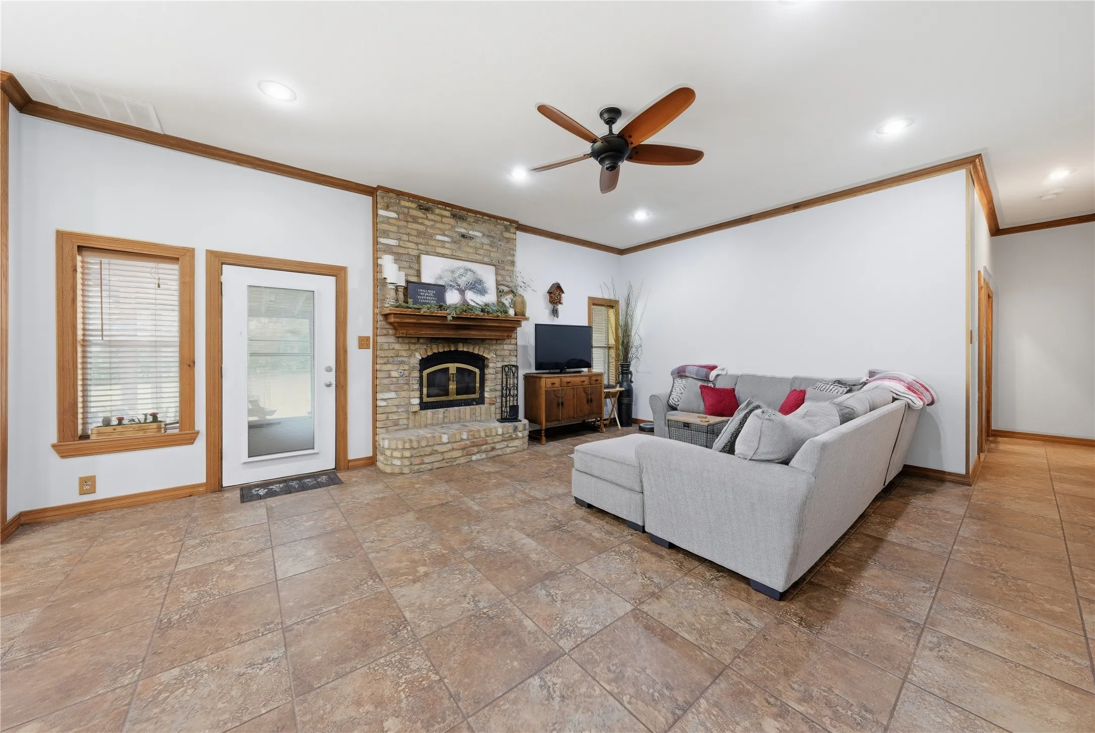 Spacious living area featuring a brick fireplace with a wood mantel, tile flooring, and wood-trimmed windows