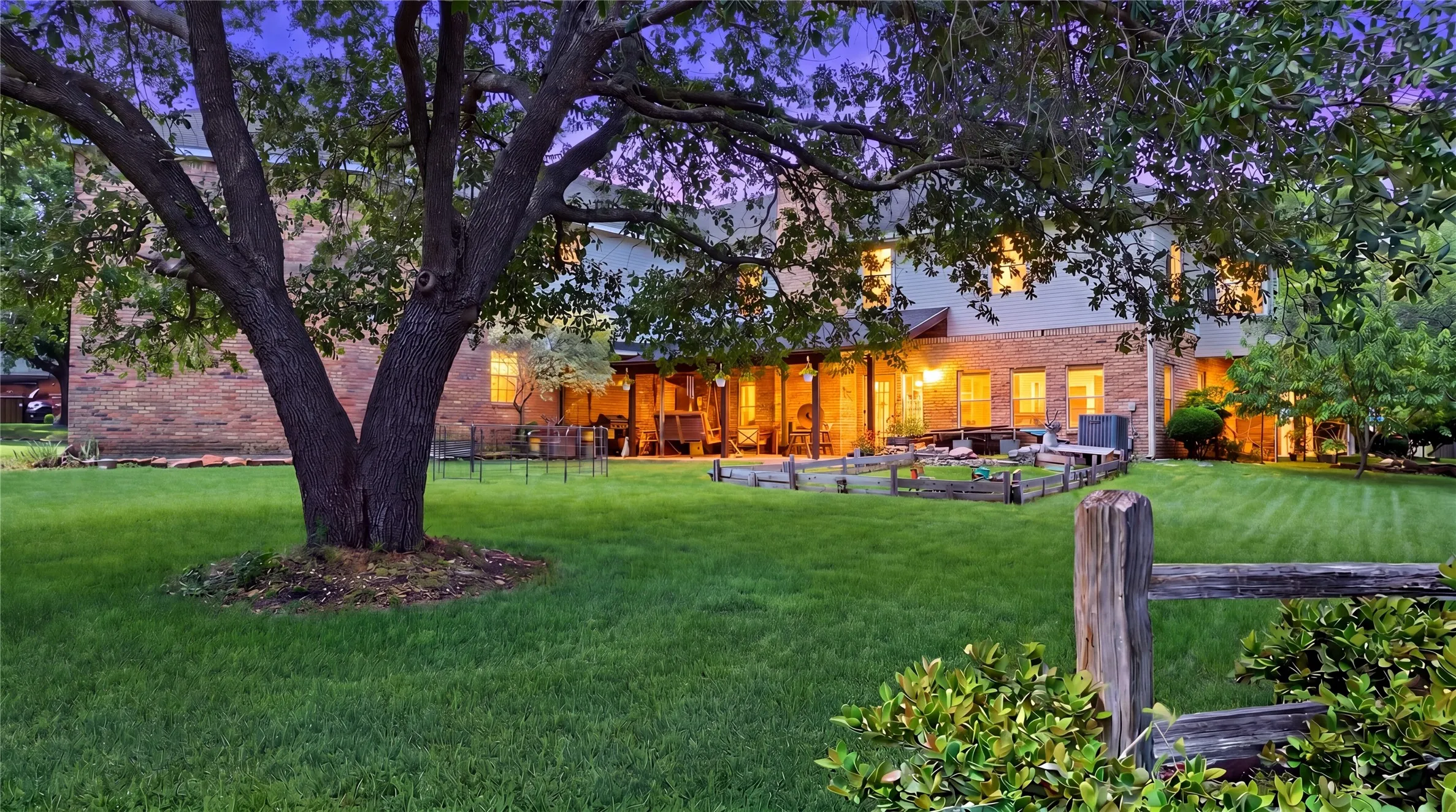 Expansive backyard featuring a mature tree, vibrant green lawn, and a split-rail fence