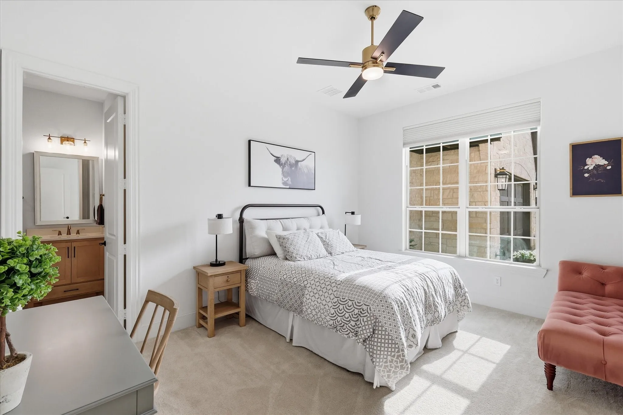 Well-lit interior room featuring a large window with white grilles, a ceiling fan with gold and black accents, and plush carpeting