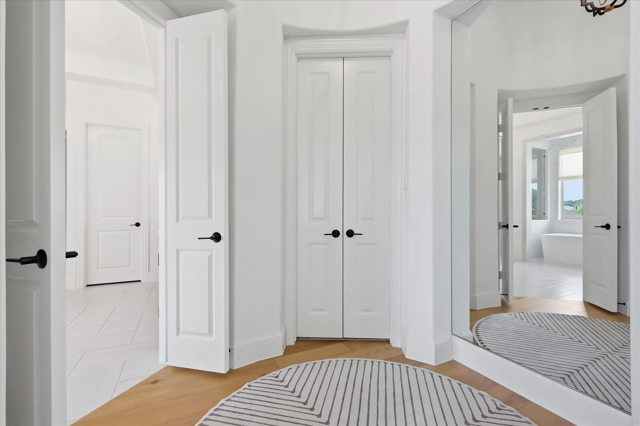 Hallway with light wood-finish flooring, white paneled doors with matte black hardware, and a full-length mirror