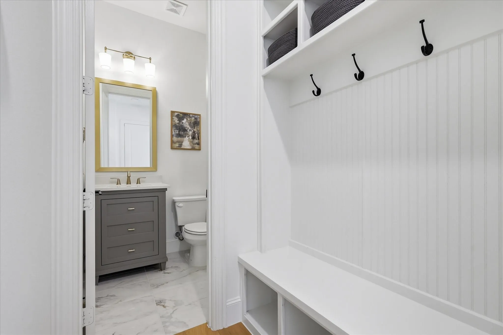 Entryway mudroom with white beadboard wall paneling, built-in bench seating, and overhead storage shelves