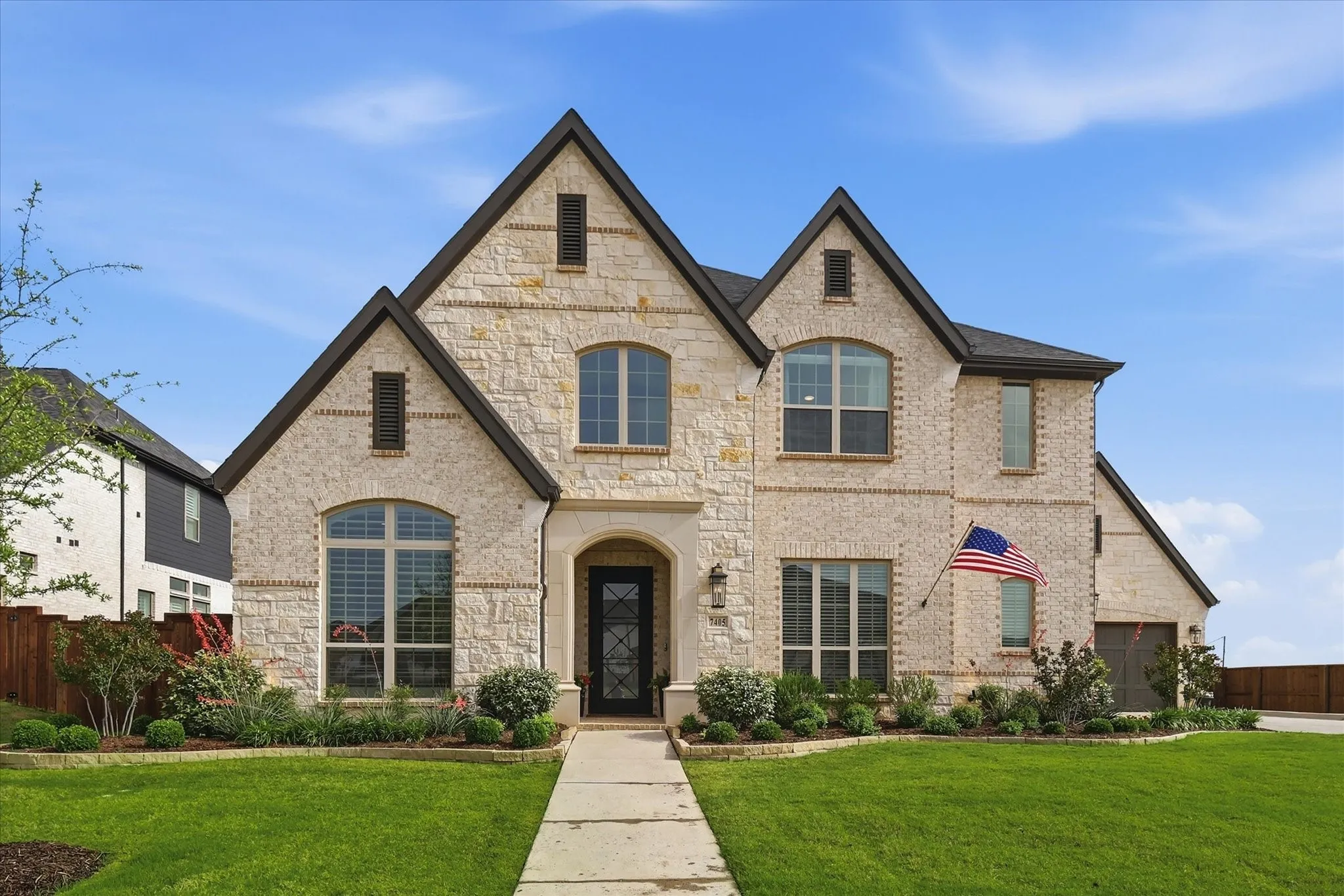 Stone veneer exterior with dark gabled rooflines, arched entry, and a prominent front door with decorative glass