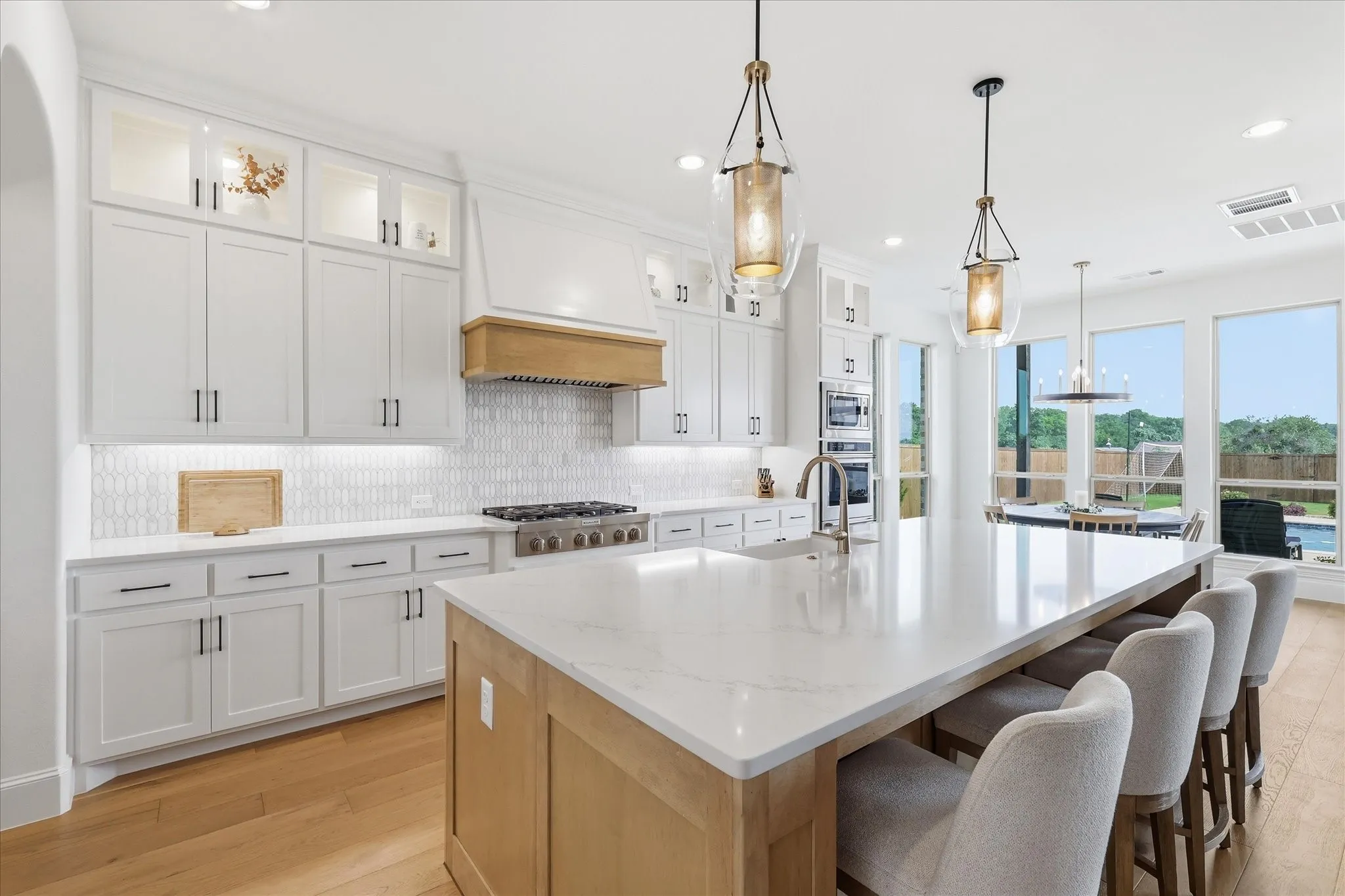 Gourmet kitchen featuring a large central island with seating, pendant lighting, white cabinetry with display uppers, stainless steel appliances, and a tiled backsplash