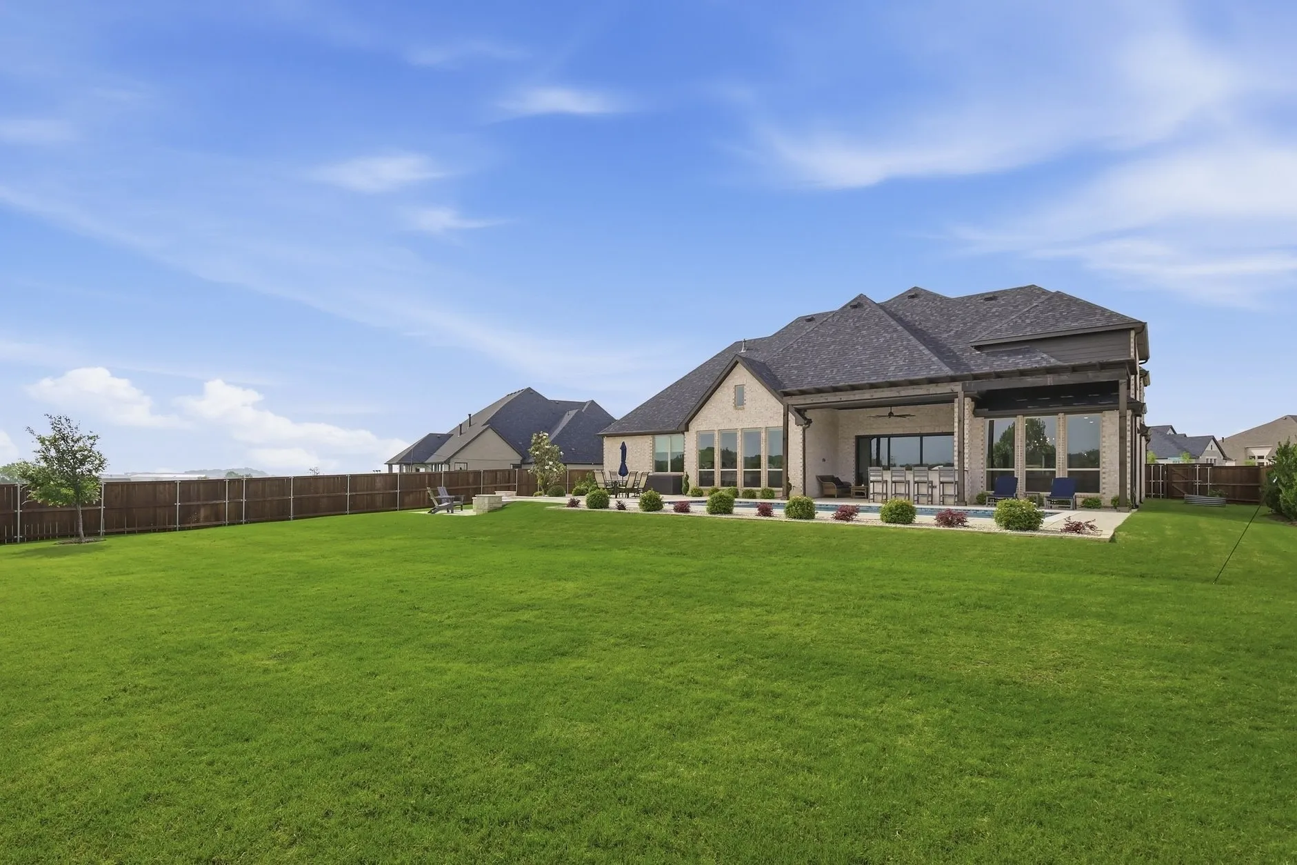Spacious backyard featuring a large green lawn, privacy fencing, a covered patio, and an in-ground swimming pool
