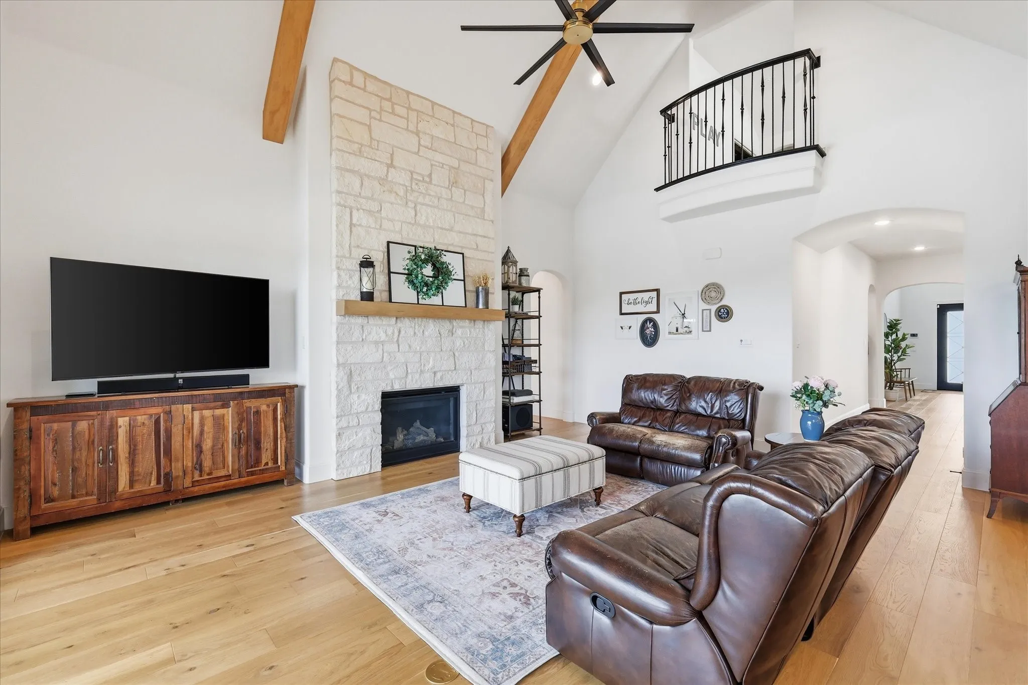 Spacious living area featuring a vaulted ceiling with exposed wood beams, a stone-faced fireplace with a wood mantel, and light wood-finish flooring