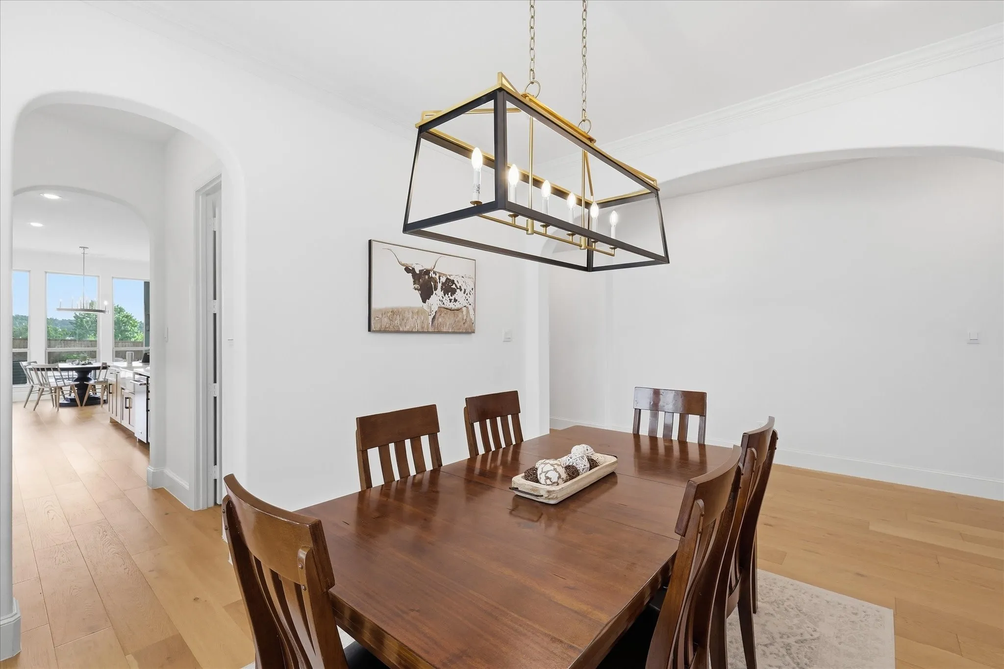 Dining area featuring a linear chandelier with a black and brass finish, white walls, and wood-finish flooring