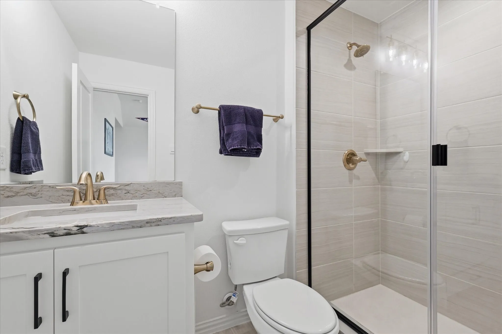 Bathroom featuring a frameless glass shower enclosure with matte black trim, a vanity with a light-toned countertop, a rectangular undermount sink, and brass-finish fixtures