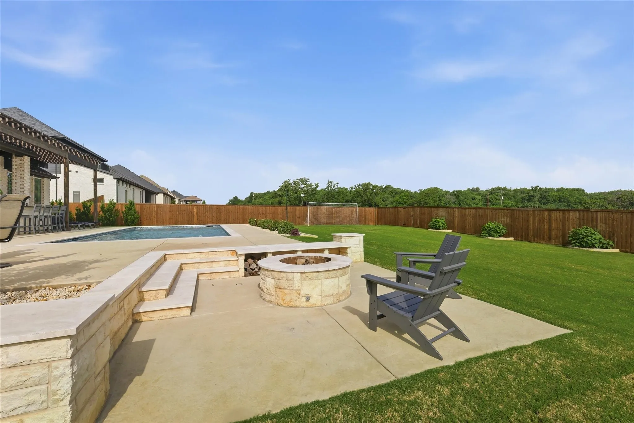 Expansive backyard featuring a rectangular swimming pool, a built-in stone fire pit, tiered stone retaining walls, and a wood privacy fence