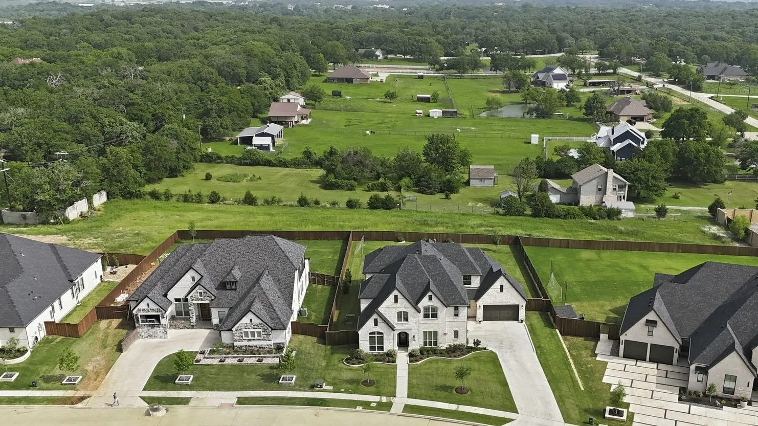 Aerial view of the Front exterior featuring a stone exterior, an attached 4-car garage, driveway, and a fenced backyard