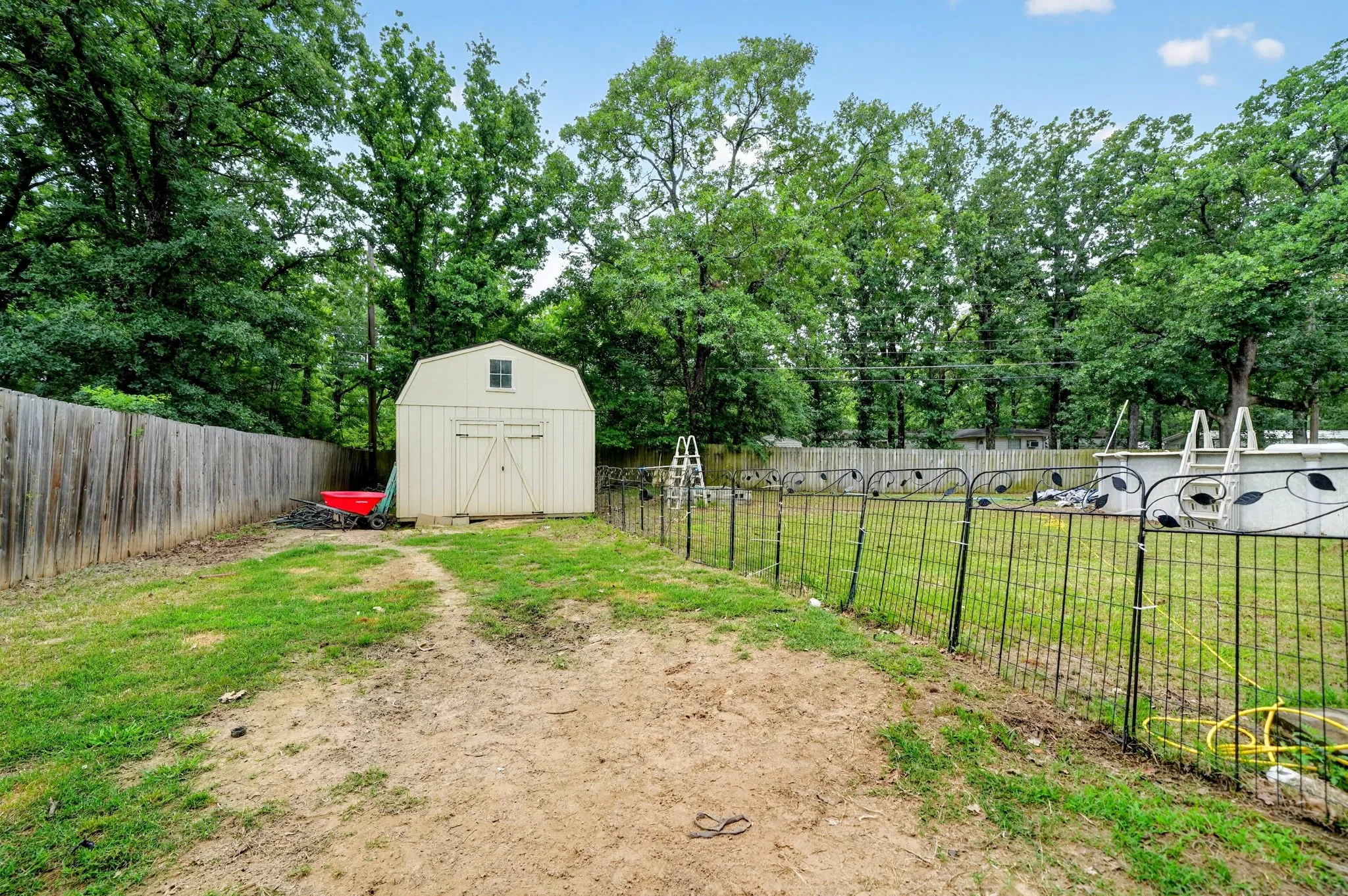 Expansive backyard featuring a storage shed with a gabled roof, an above-ground pool, a wooden privacy fence, and a decorative metal fence