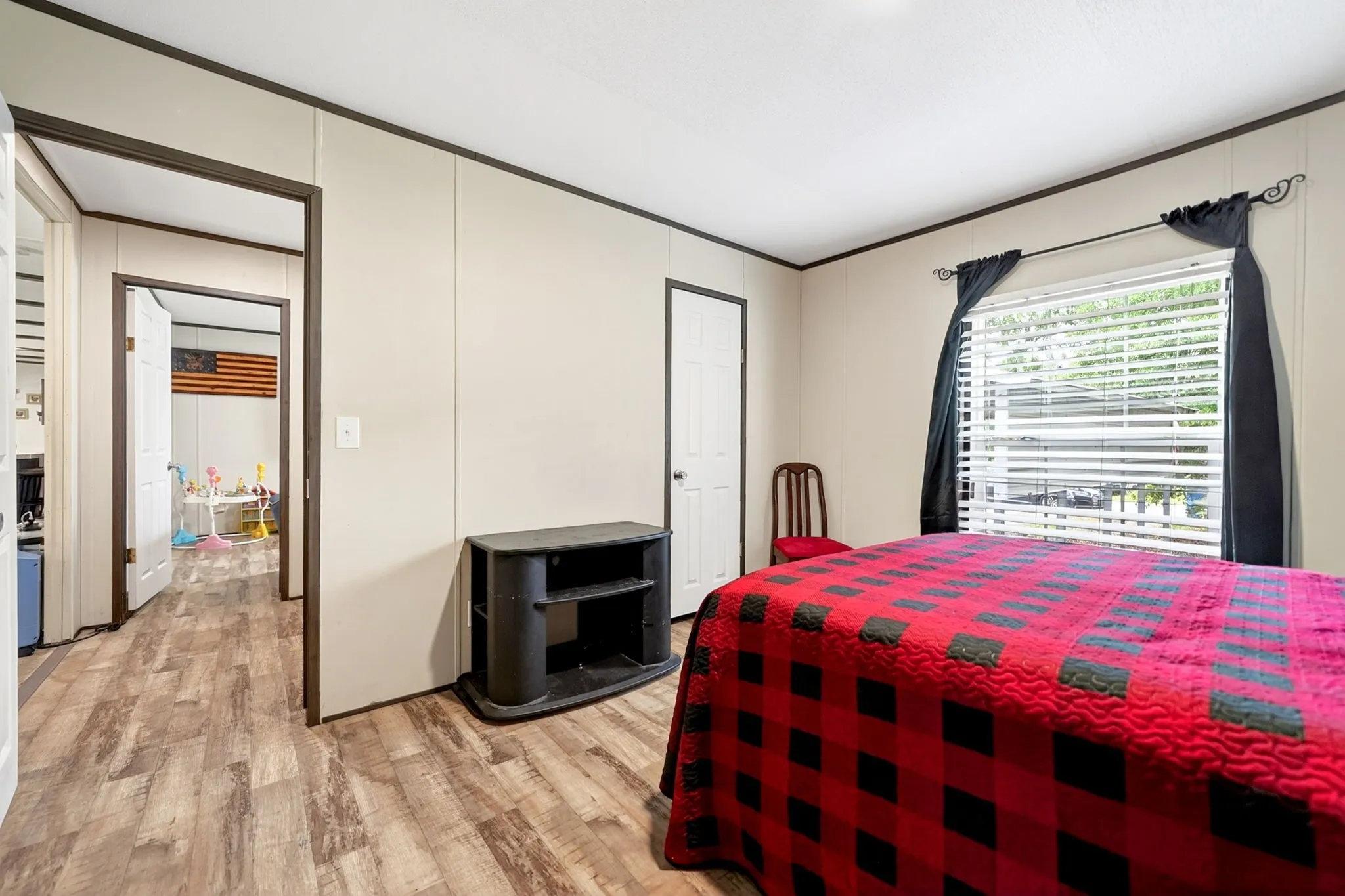 Bedroom with wood-finish flooring, light neutral walls, and a window featuring horizontal blinds