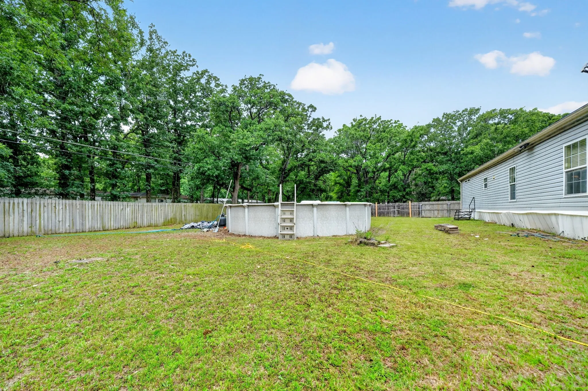 Expansive backyard featuring an above-ground pool, a privacy fence, and mature trees along the perimeter