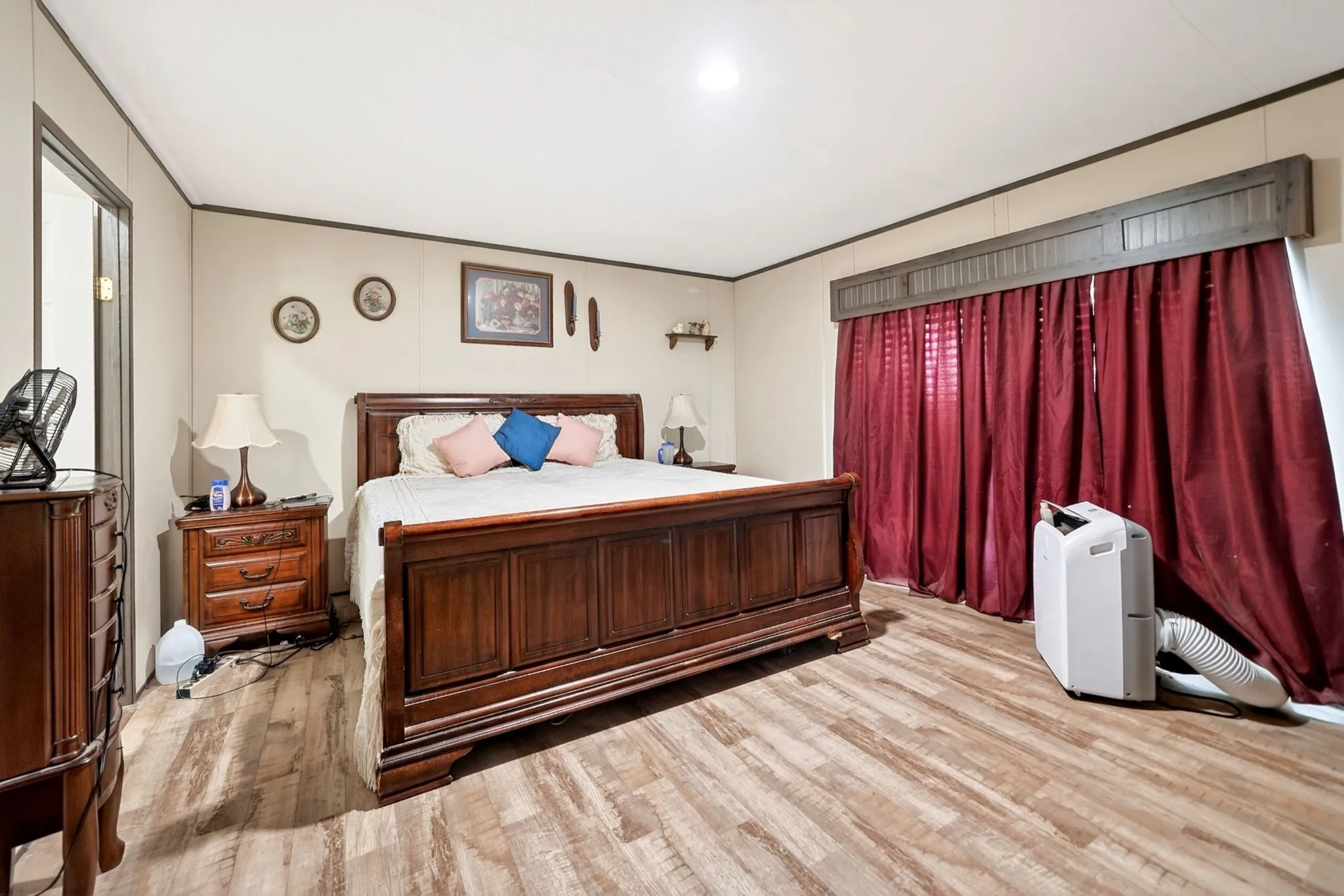 Spacious room featuring wood-finish flooring, light-toned walls, and a window with a decorative valance