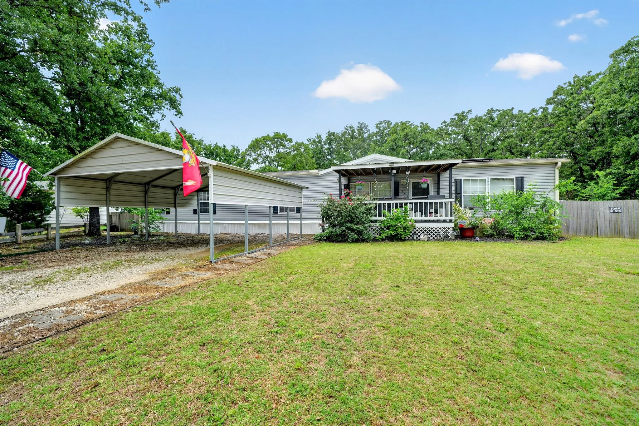 Manufactured home featuring a covered front porch with white railings, a gravel driveway, and an attached metal carport
