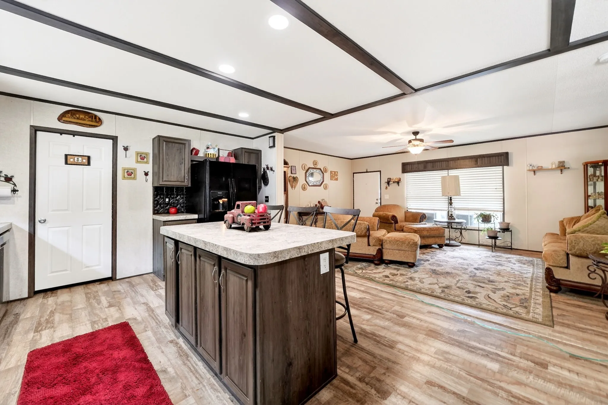 Open-concept living space featuring a kitchen island with seating, wood-finish flooring, a ceiling fan, and decorative ceiling beams