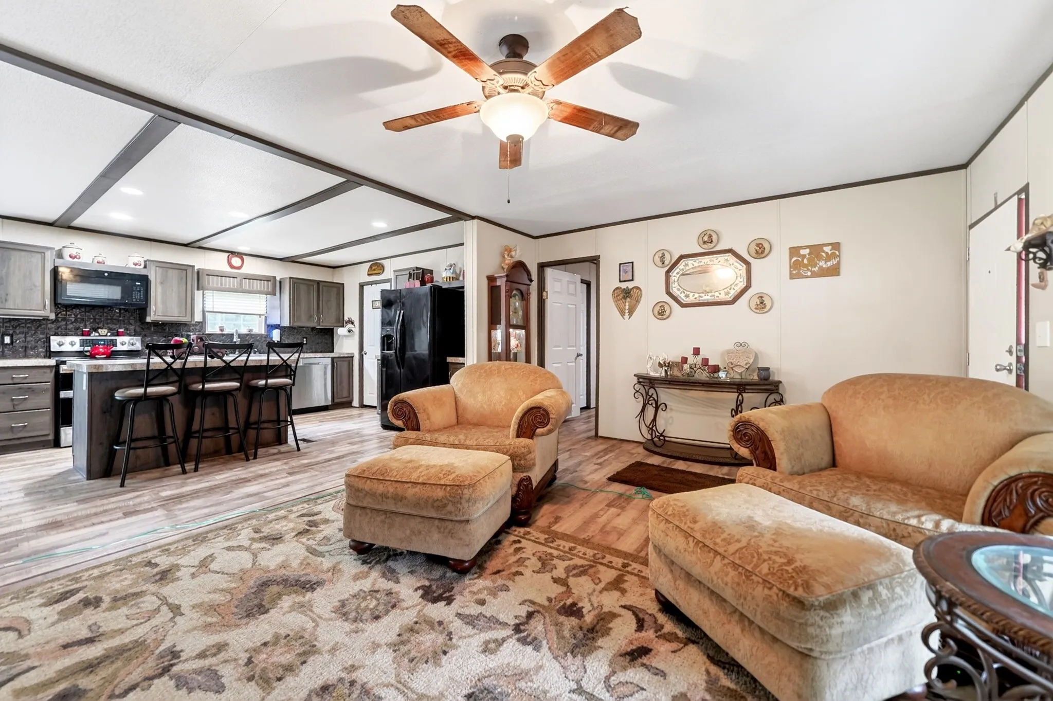 Open-concept living space featuring wood-finish flooring, a kitchen island with seating, dark shaker-style cabinetry, and a ceiling fan with integrated lighting