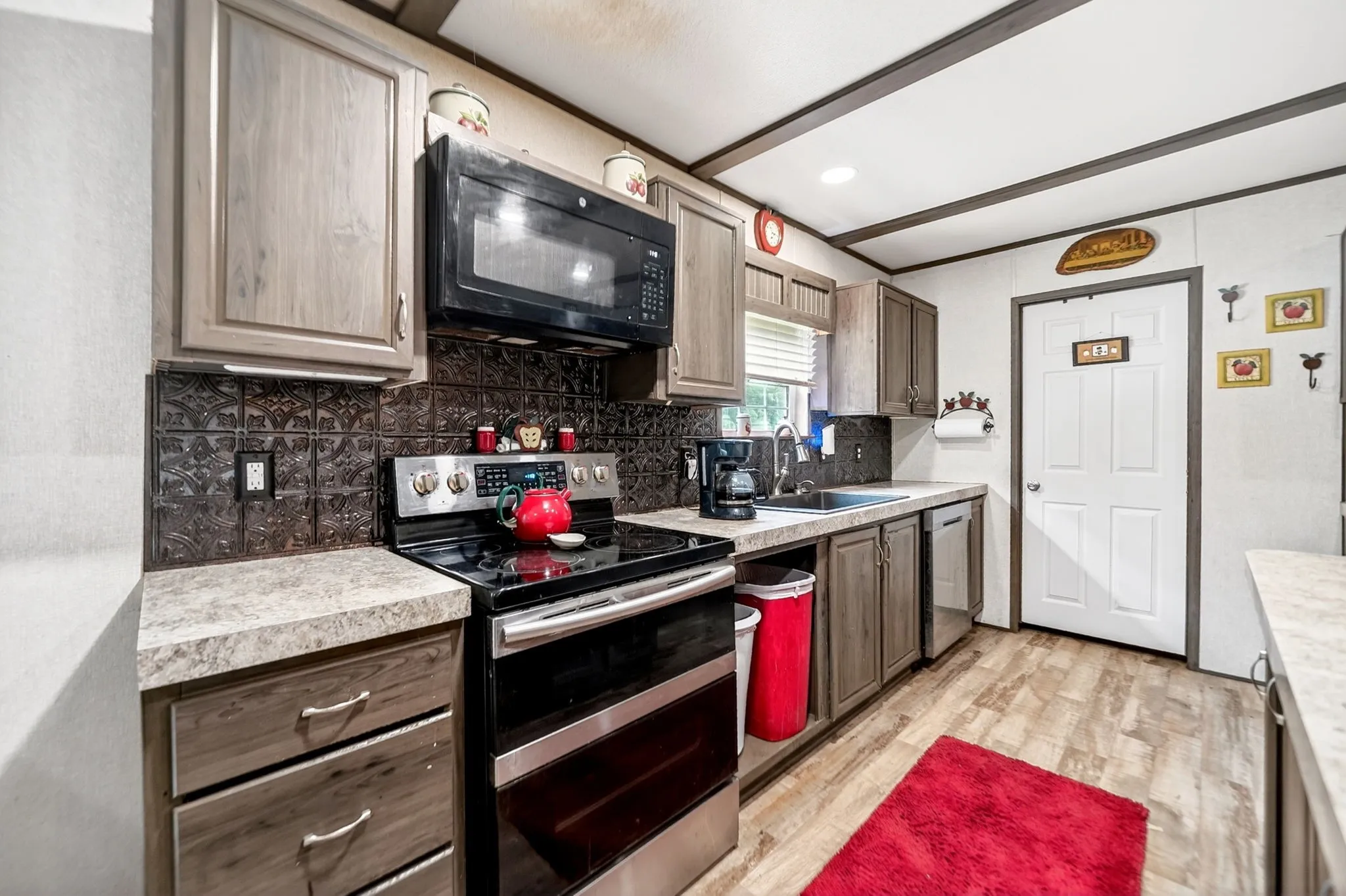 Kitchen featuring wood-finish flooring, light-toned cabinetry, dark patterned backsplash, stainless steel appliances, and a compact dishwasher
