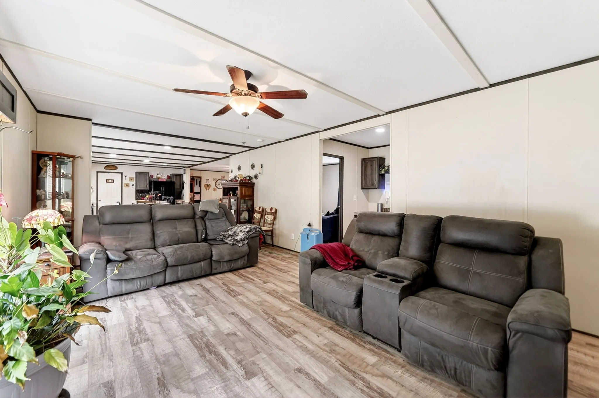 Spacious living area featuring wood-finish flooring, a ceiling fan with integrated lighting, and neutral wall paneling