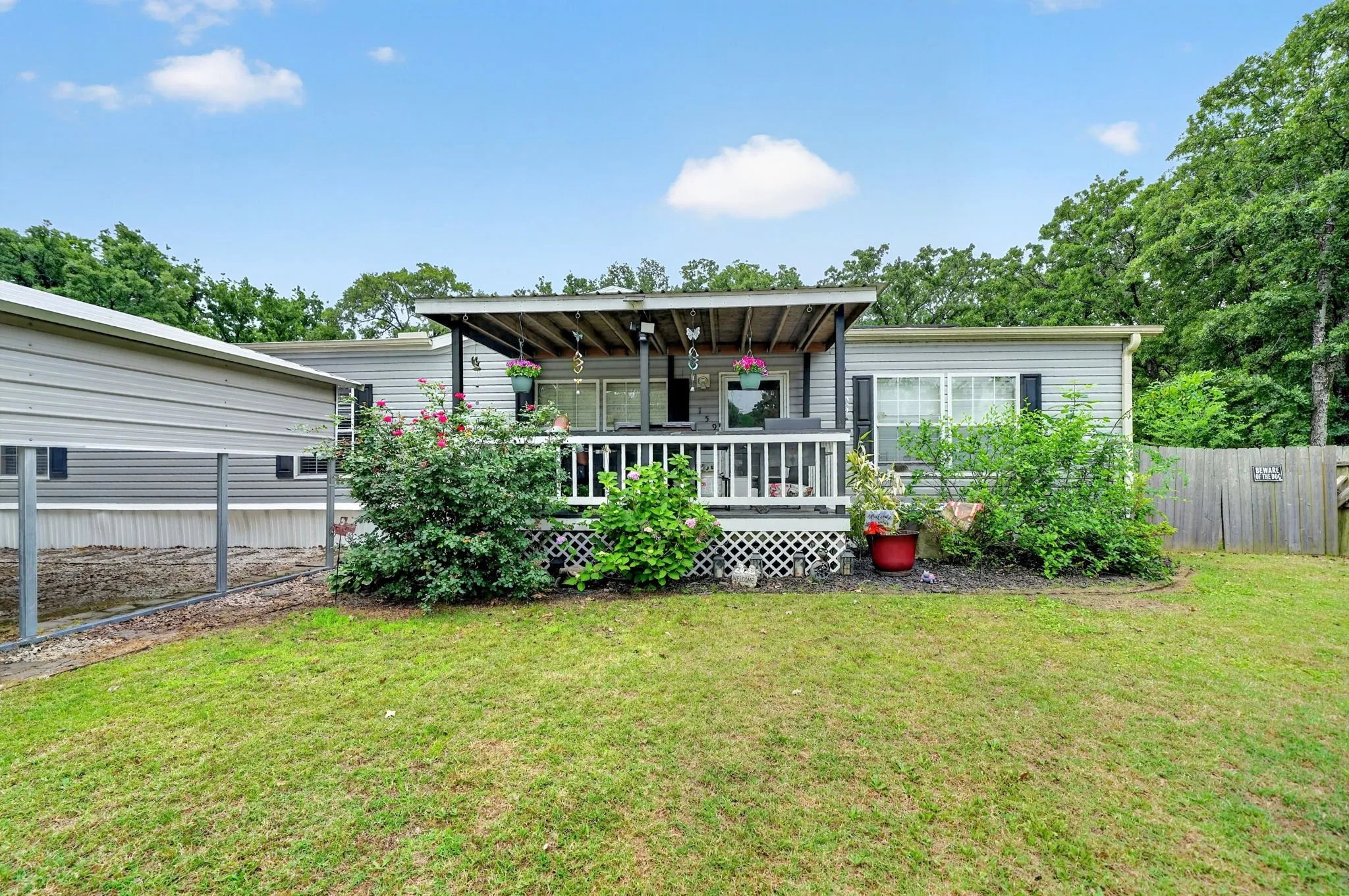 Rear exterior featuring a covered deck with white railing, sliding glass doors, and mature landscaping