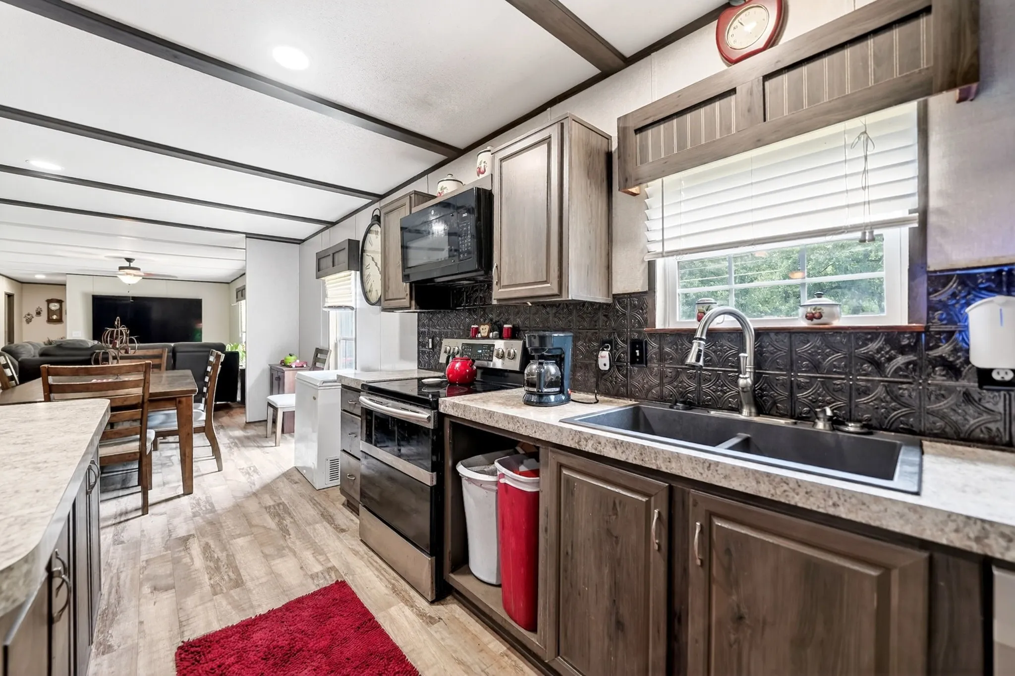 Kitchen featuring wood-finish flooring, dark-stained cabinetry, light-toned countertops, a built-in microwave, and a double basin sink with a gooseneck faucet