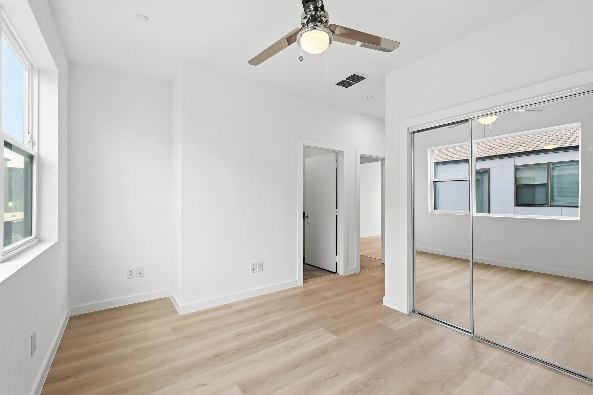 Light-filled interior featuring expansive window, wood-finish flooring, mirrored closet doors, contemporary ceiling fan, and crisp white walls