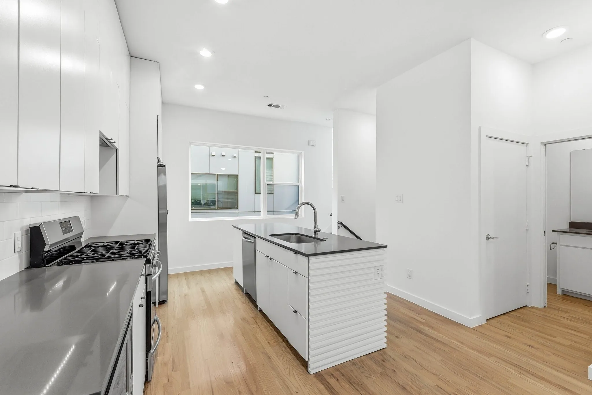 Contemporary kitchen featuring stainless steel appliances, a center island with sink, white shaker-style cabinetry, and wood-finish flooring