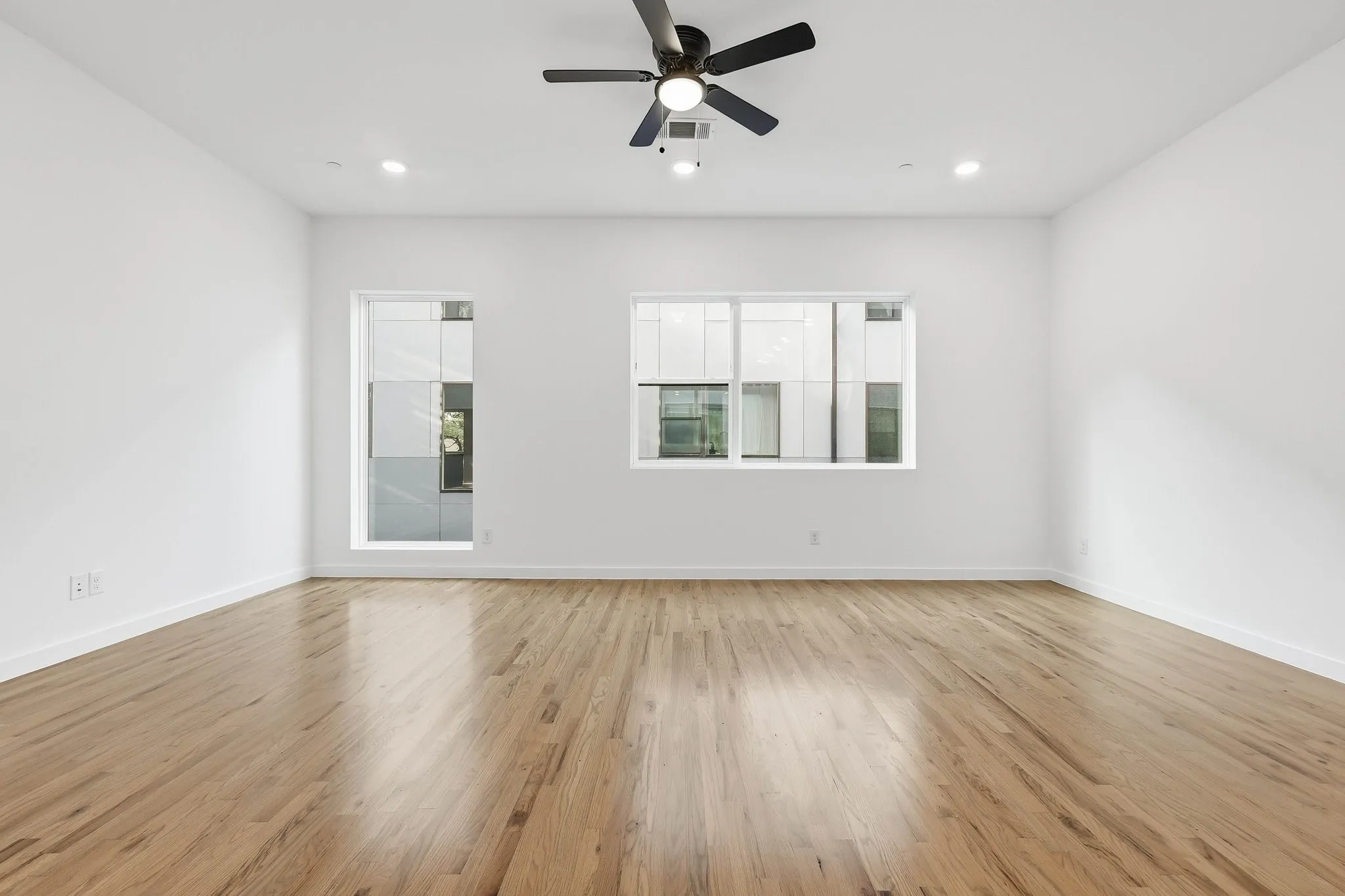 Spacious room with wood-finish flooring, white walls, and a ceiling fan