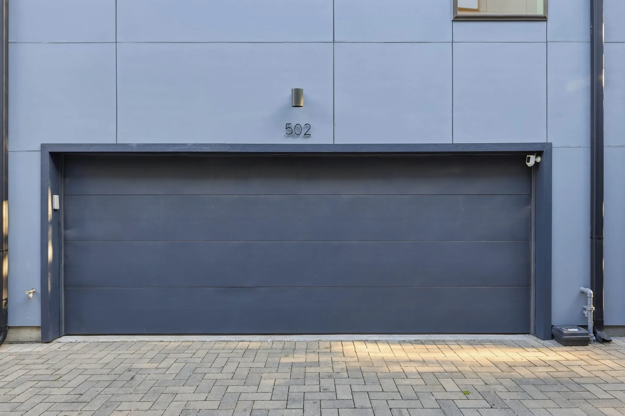 Modern gray garage door with sleek paneling, integrated wall sconces, and a paver driveway