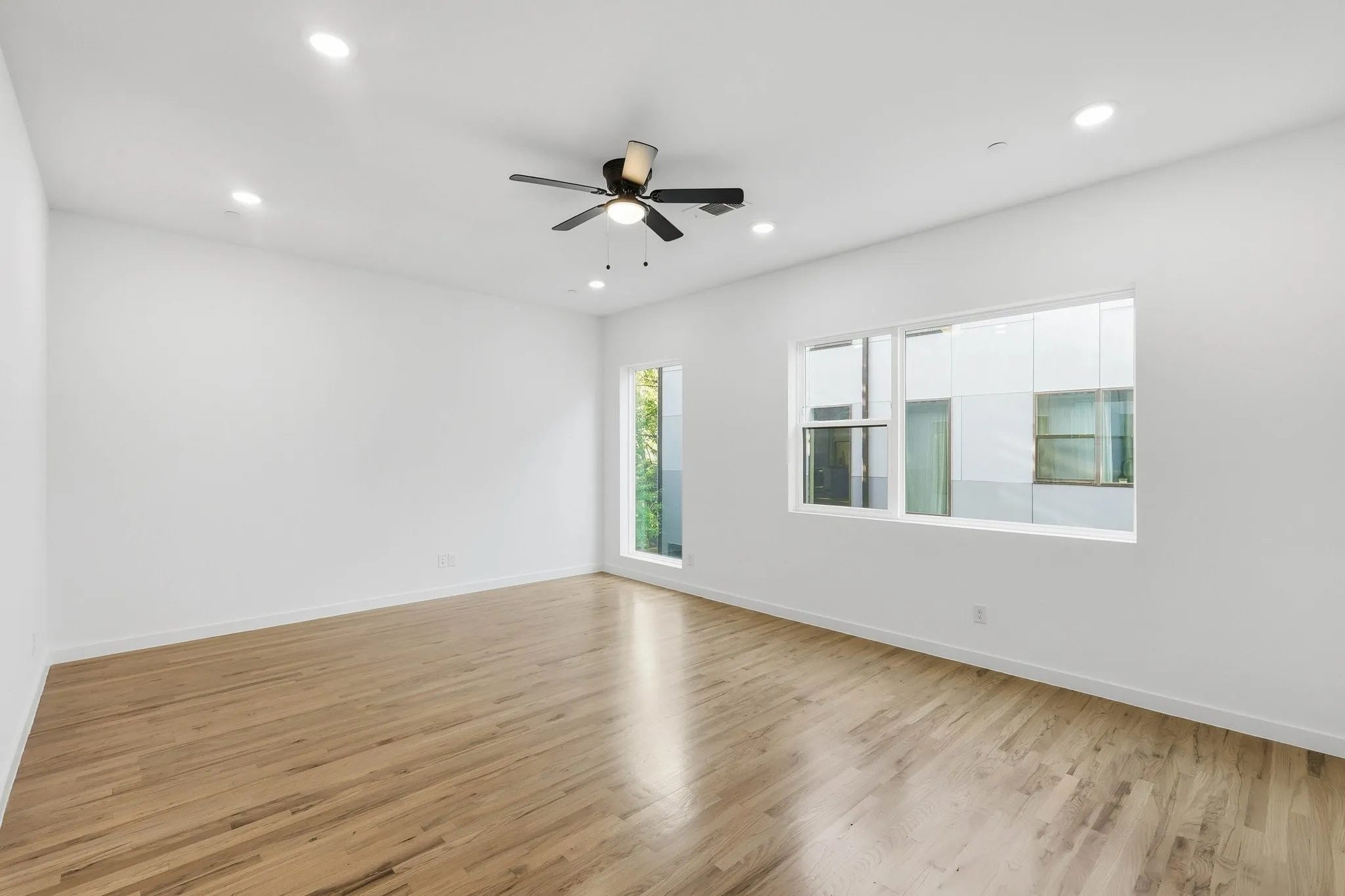 Spacious interior room featuring wood-finish flooring, a modern ceiling fan, multiple recessed lights, and large windows