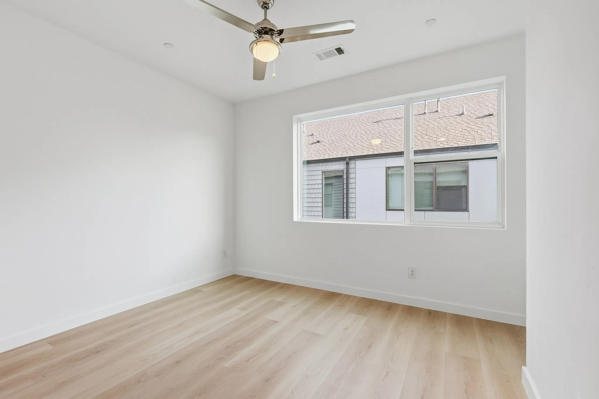 Bright room featuring a large window, light wood-finish flooring, white baseboards, and a ceiling fan with integrated lighting