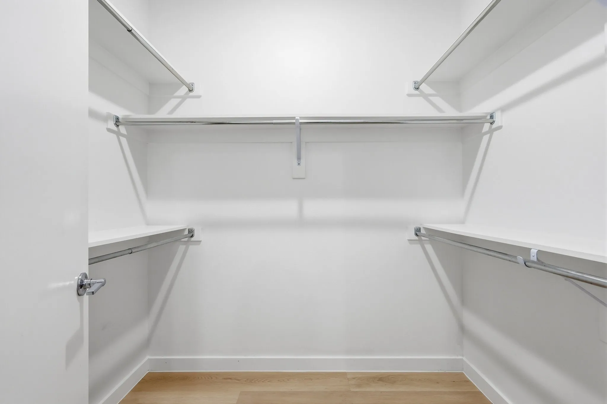 Walk-in closet featuring light wood-finish flooring, white walls, and chrome hanging rods