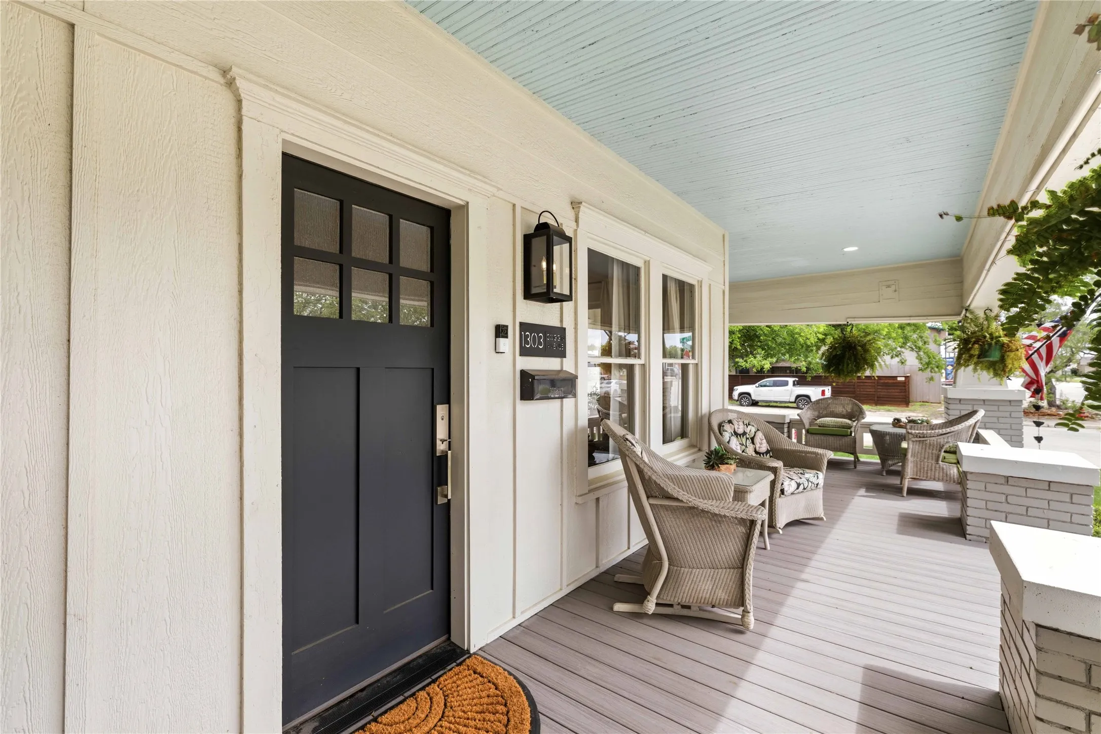 Inviting front porch featuring a dark paneled entry door with transom windows, board and batten siding, beadboard ceiling, and gray wood-finish decking
