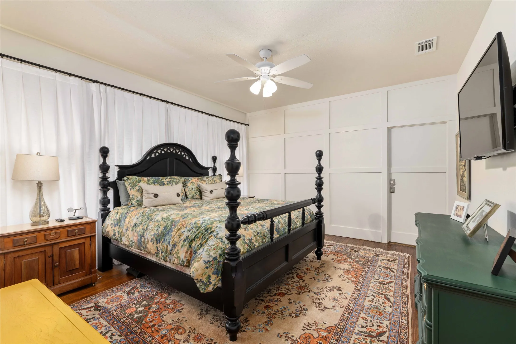 Bedroom featuring dark wood-finish flooring, white ceiling fan, and panel molding accent wall