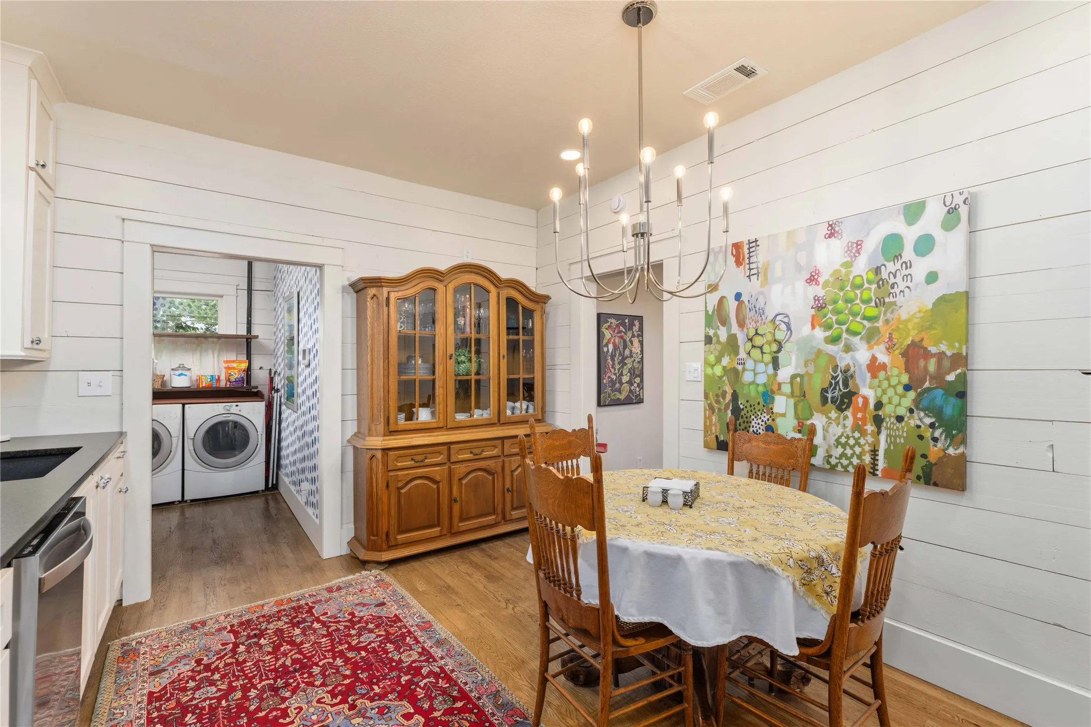 Dining area featuring wood-finish flooring, shiplap walls, and a contemporary chandelier