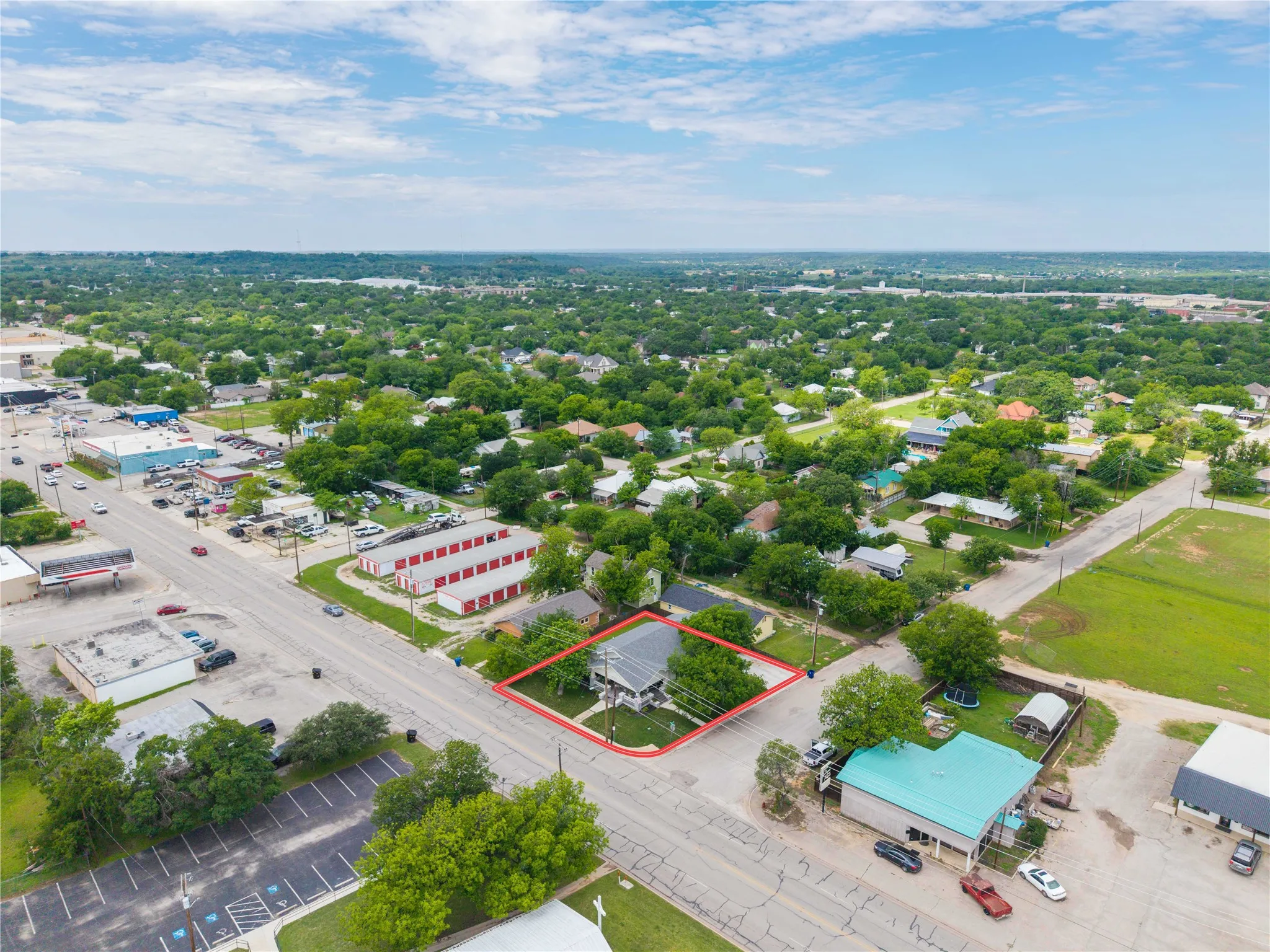 Corner lot property featuring a light-colored exterior, an asphalt shingle roof, and surrounding mature trees